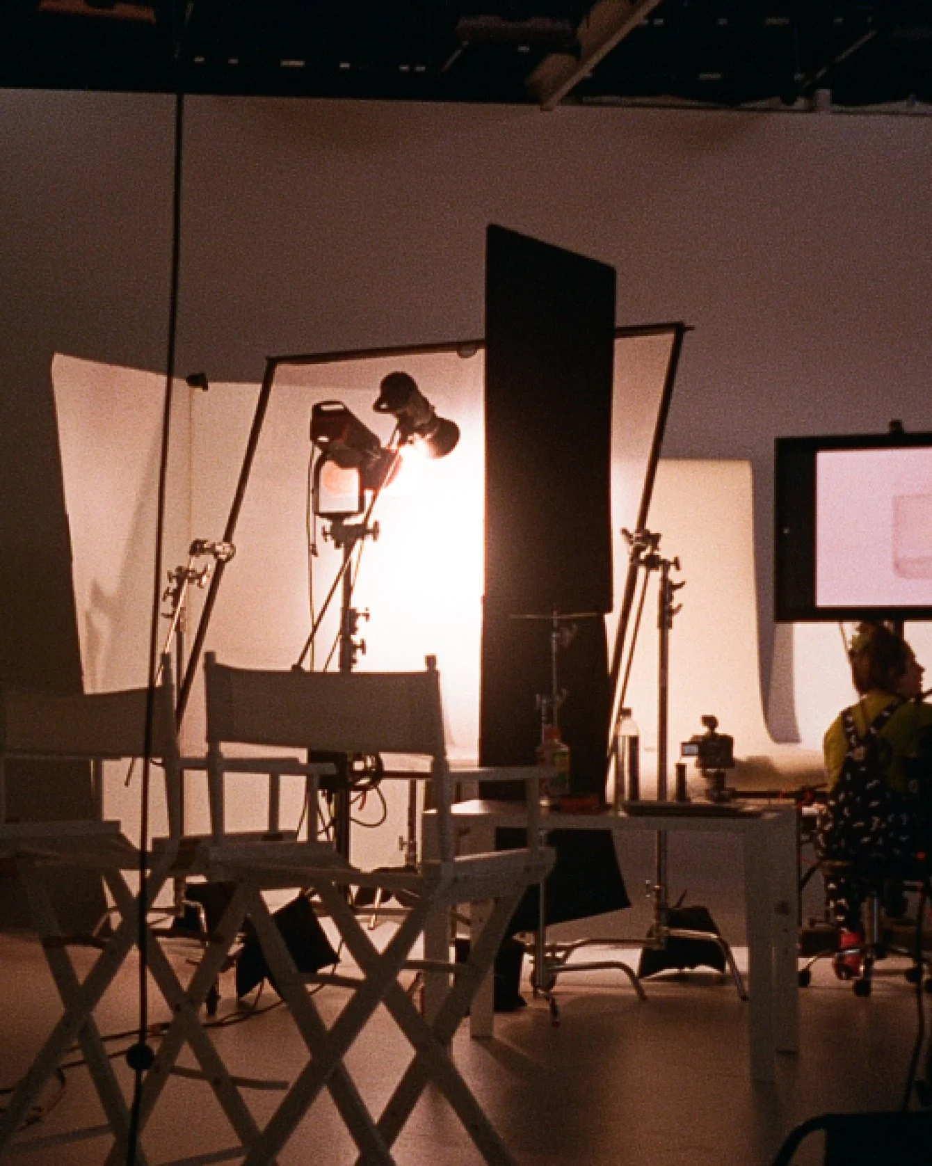 Interior of a photography studio with lighting equipment, backdrop, and a person sitting at a workstation.