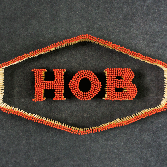 Arrangement of red matchsticks spelling out 'HOB' on a dark background, with a border of matchsticks surrounding the text.