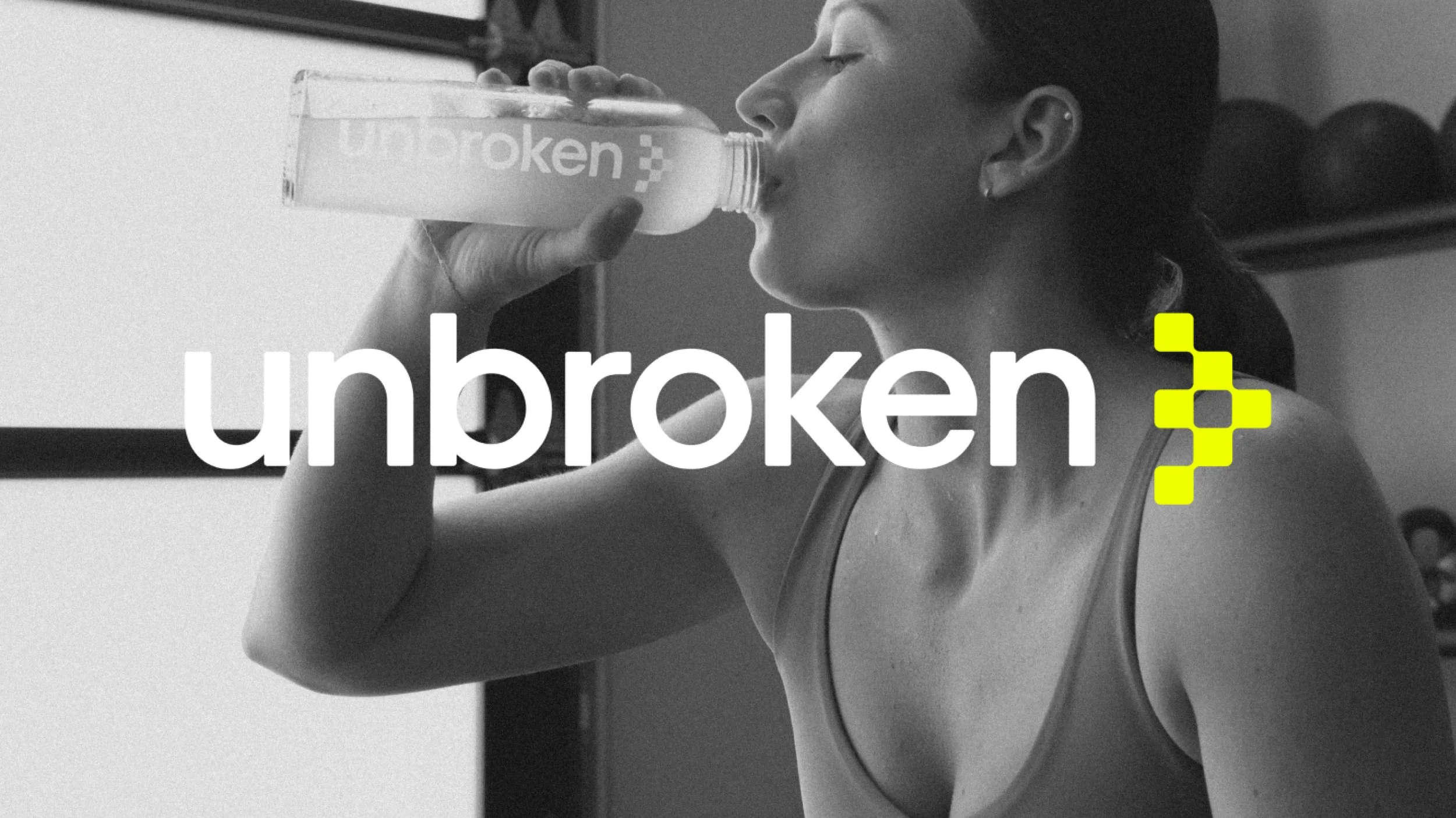 A woman drinking water from a bottle with the 'unbroken' logo in the foreground, in black and white.
