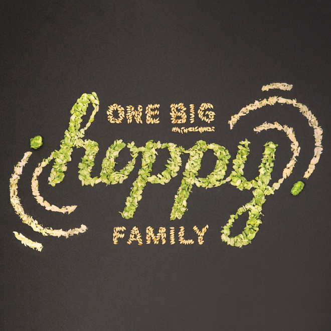 Text created with green and beige flower petals on a dark background reading 'One Big Happy Family' with a heart symbol.