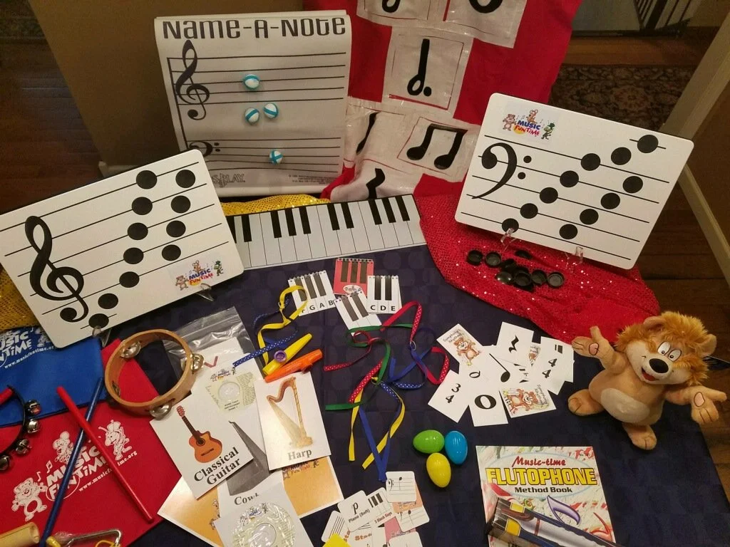 A collection of children's music learning materials including musical note cards, toy instruments, colorful eggs, a stuffed bear, and a music-themed book arranged on a table.