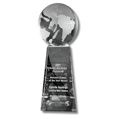 A glass trophy featuring a globe on top, engraved with text including '2021 Music Academy Success, National School of the Year Award, Camille Hastings, Leading Note Studios, Encinitas, California'.