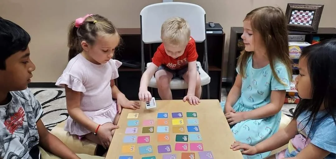 Six children gathered around a table playing a card game or activity with colorful cards.