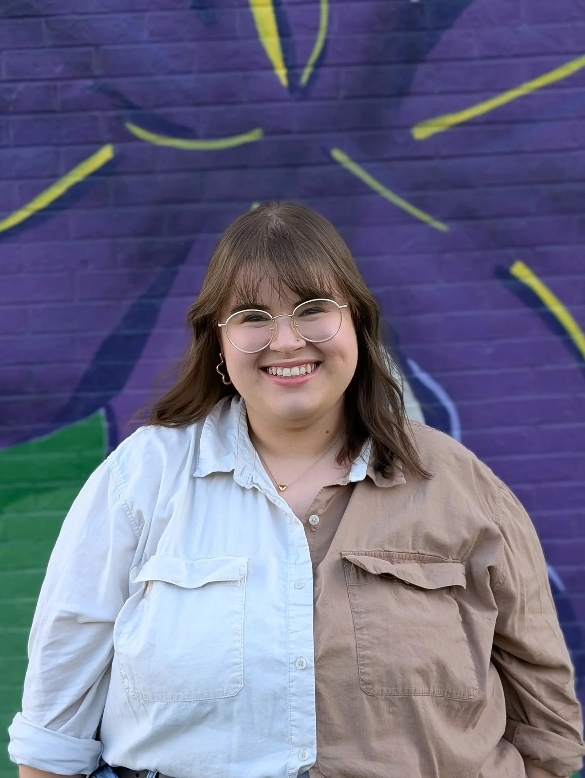 Smiling woman with brown hair and glasses in front of a purple floral mural
