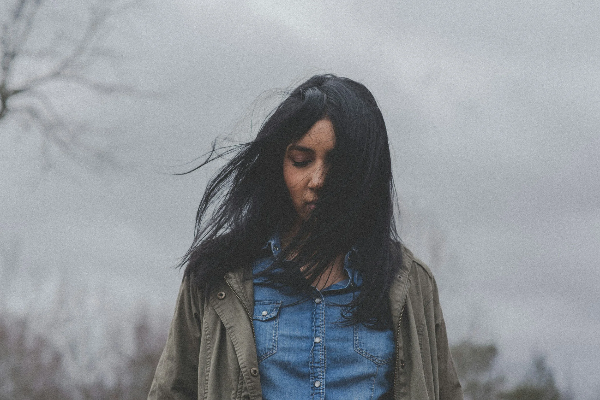 South Asian woman looking down with wind blowing her hair across her face, against a grey sky | therapy for depression in Pennsylvania