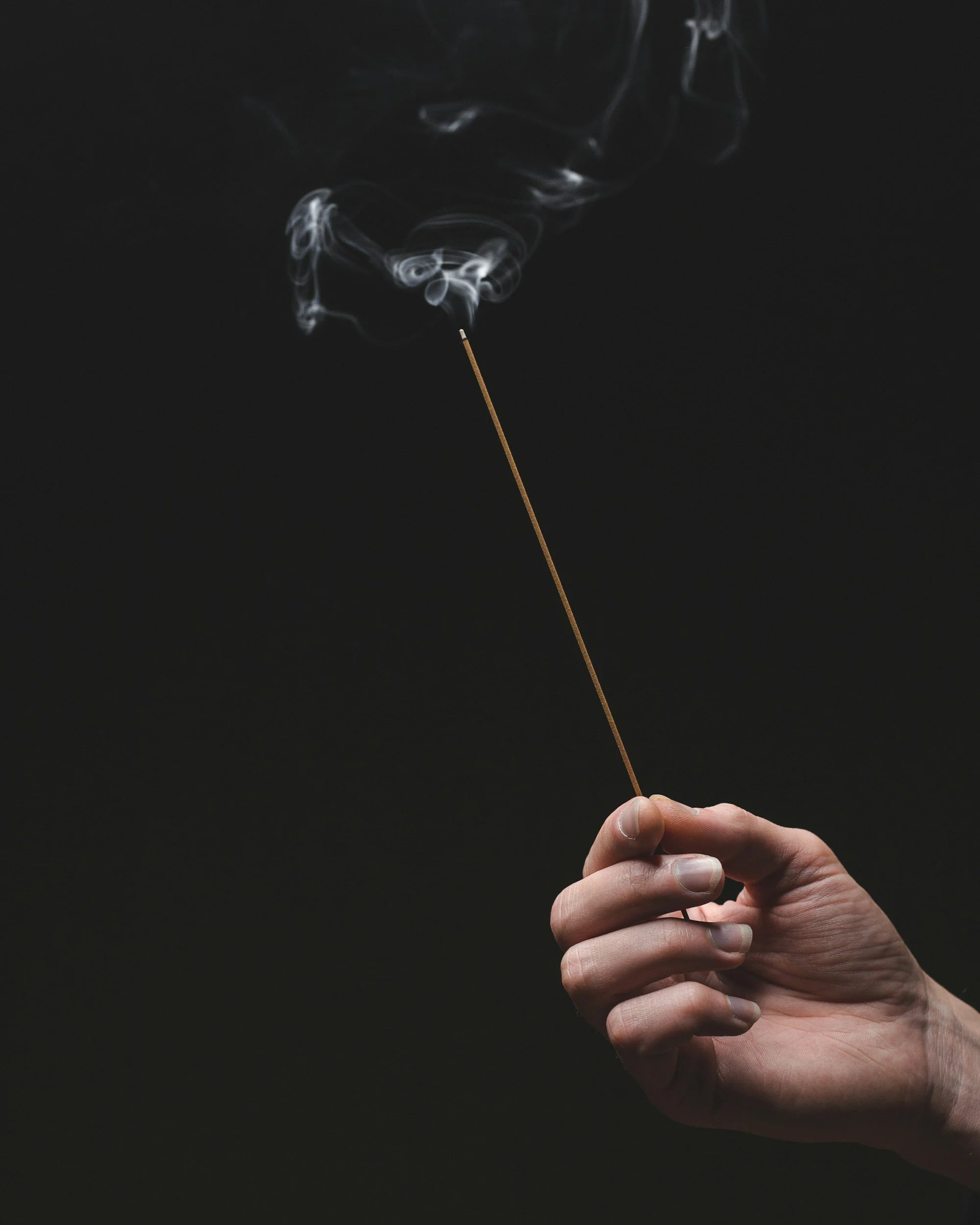 hand holding a stick of burning incense against a dark background, with smoke rising | ifs somatic therapy | pennsylvania pittsburgh philly allentown erie