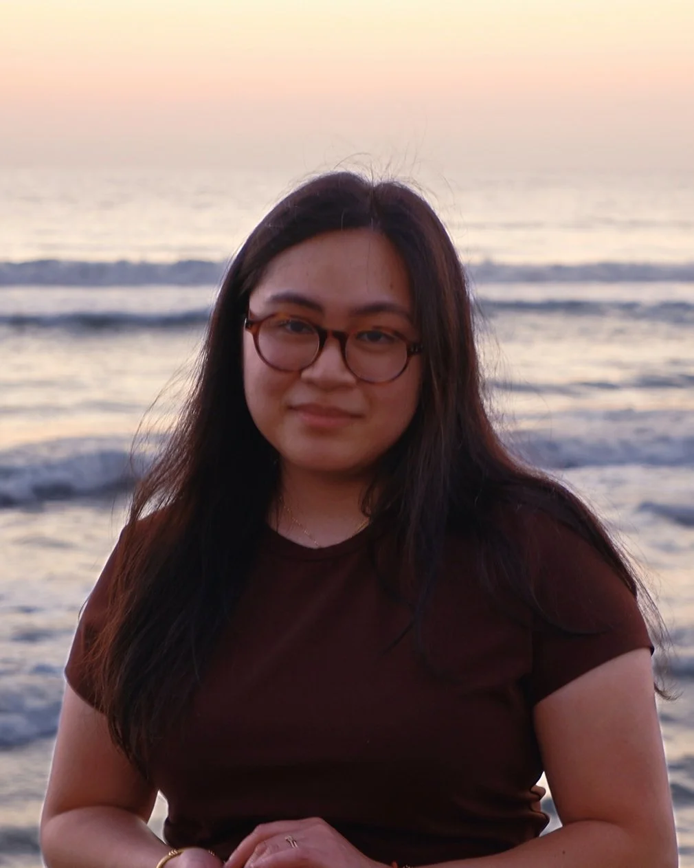 A portrait of a woman with long dark hair, wearing glasses and a black shirt, standing outdoors during sunset | chelsea adams lpc | therapist in pittsburgh philly erie allentown