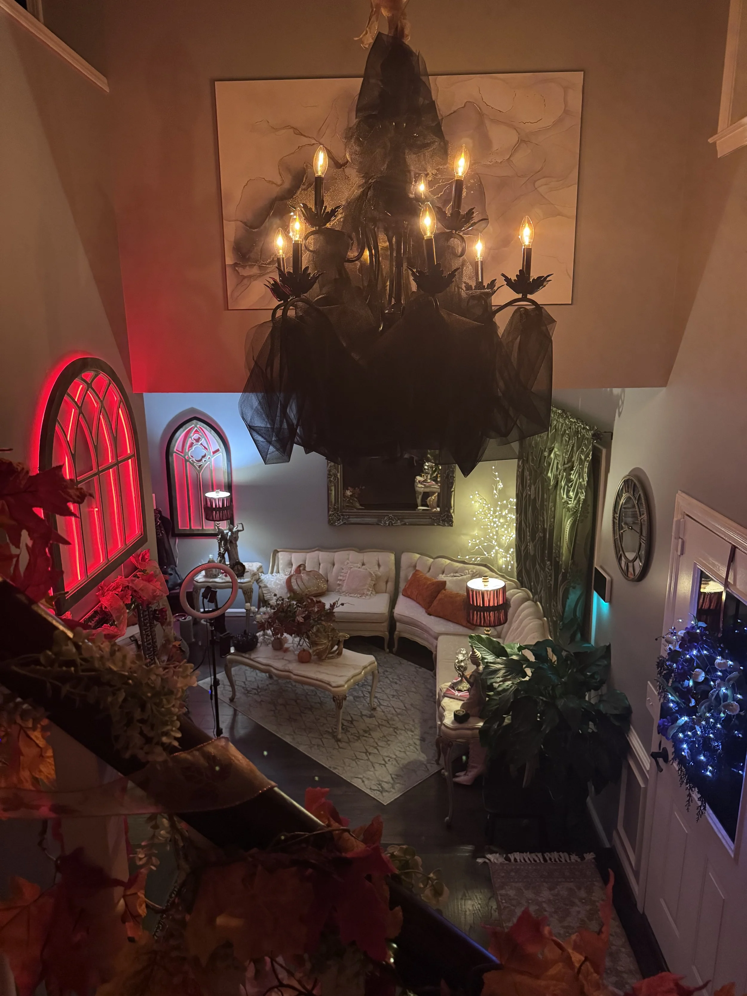 Living room decorated for the holidays with colorful lighting, a chandelier, and various furniture including couches, a coffee table, and lamps.