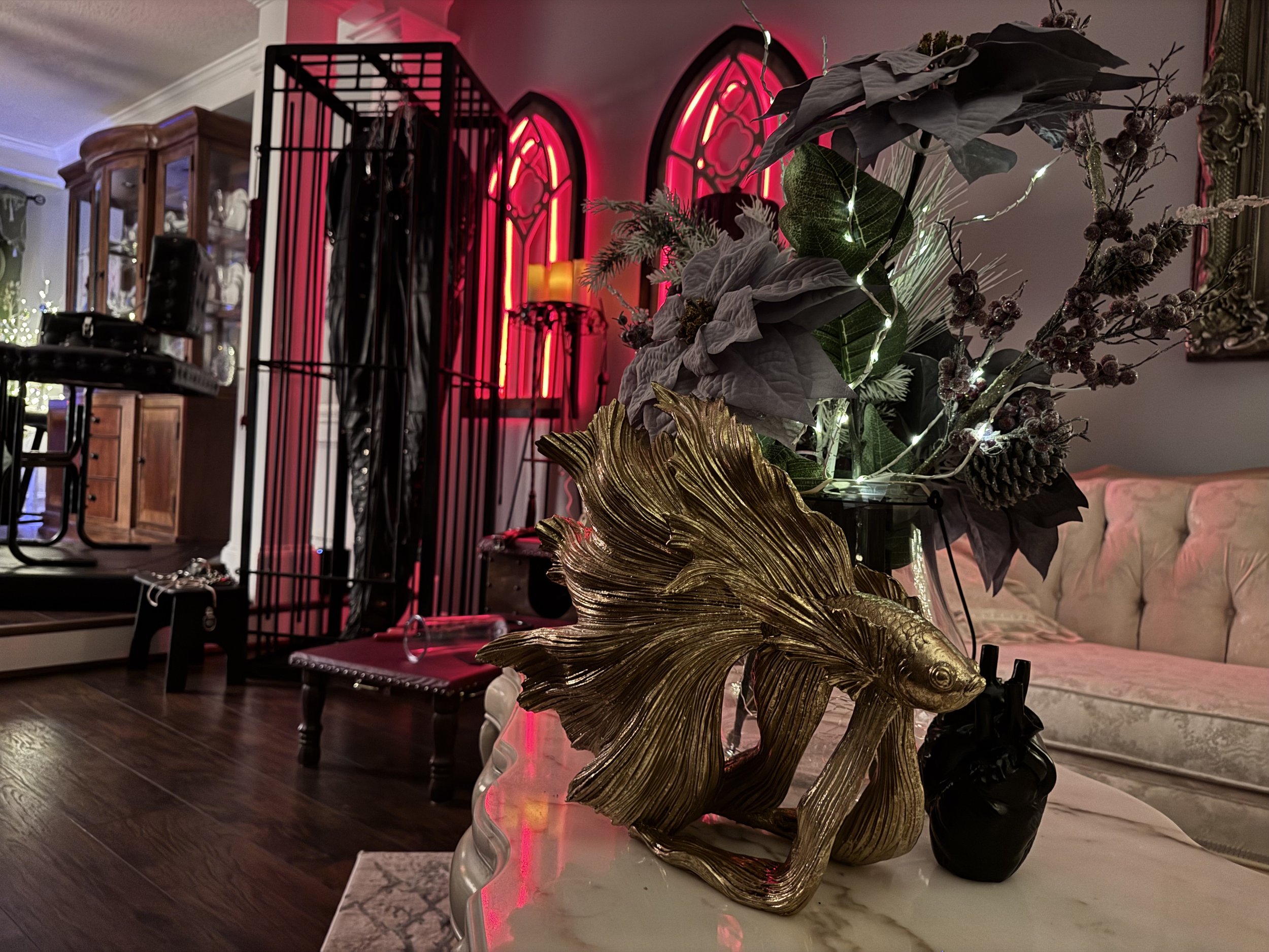 Decorative goldfish sculpture, floral arrangement with artificial flowers and lights, pink neon Gothic-style windows, and cozy living room with a pale pink tufted sofa.