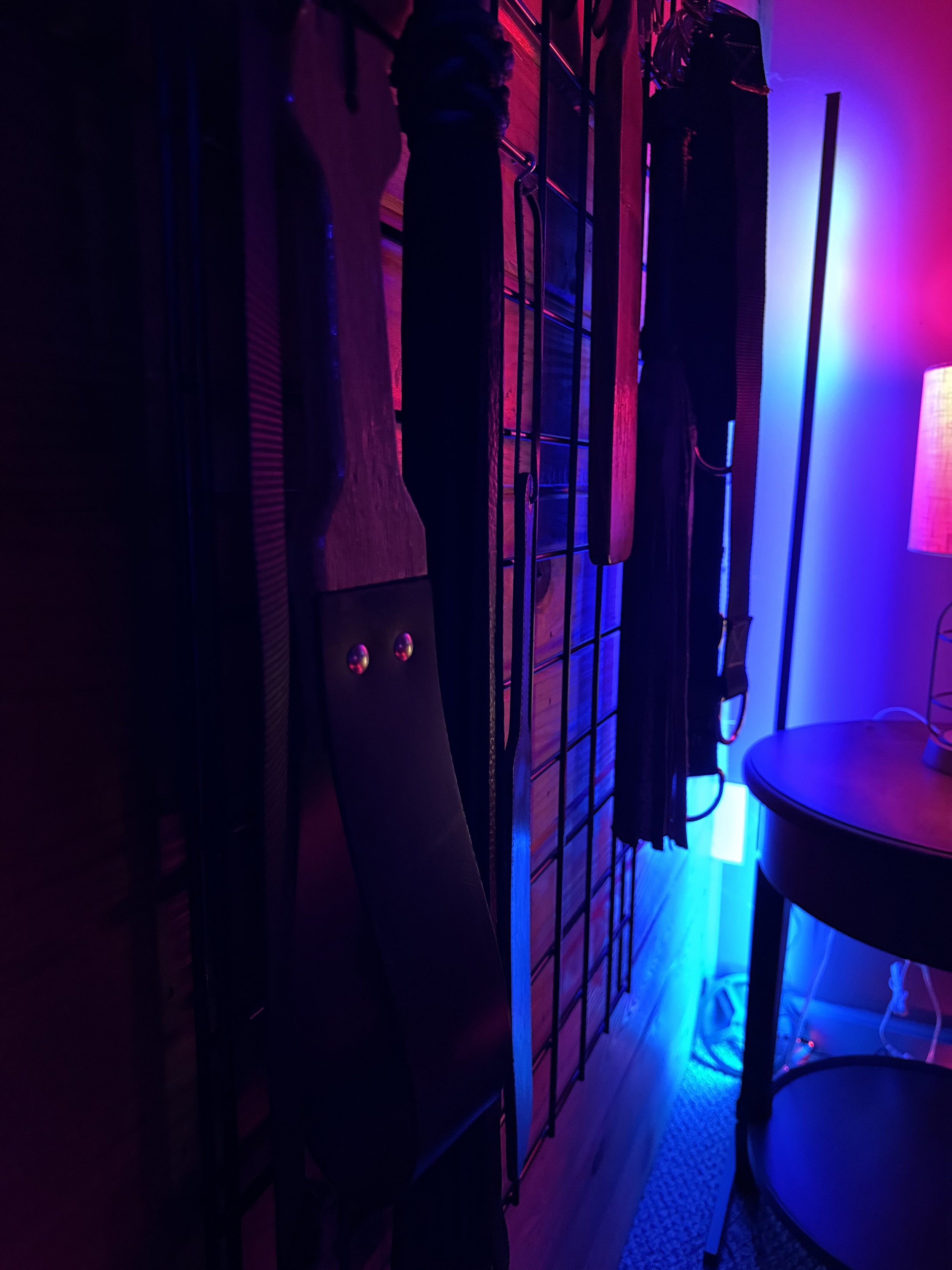 Guitar and other musical equipment hanging on a wall in a room with vibrant blue and pink lighting.