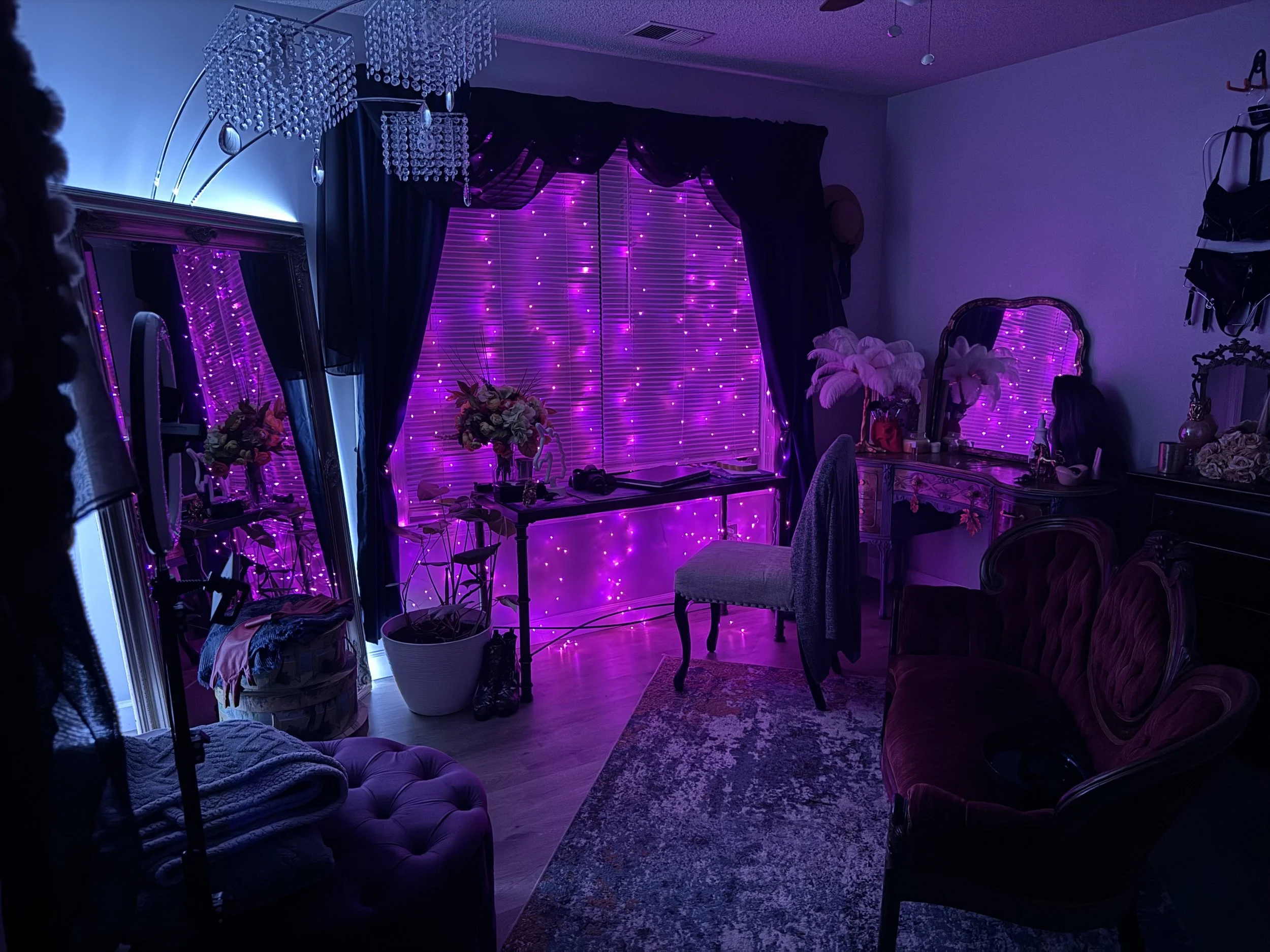 Interior room decorated with purple and pink lights, featuring vintage furniture, a large mirror, and floral arrangements.