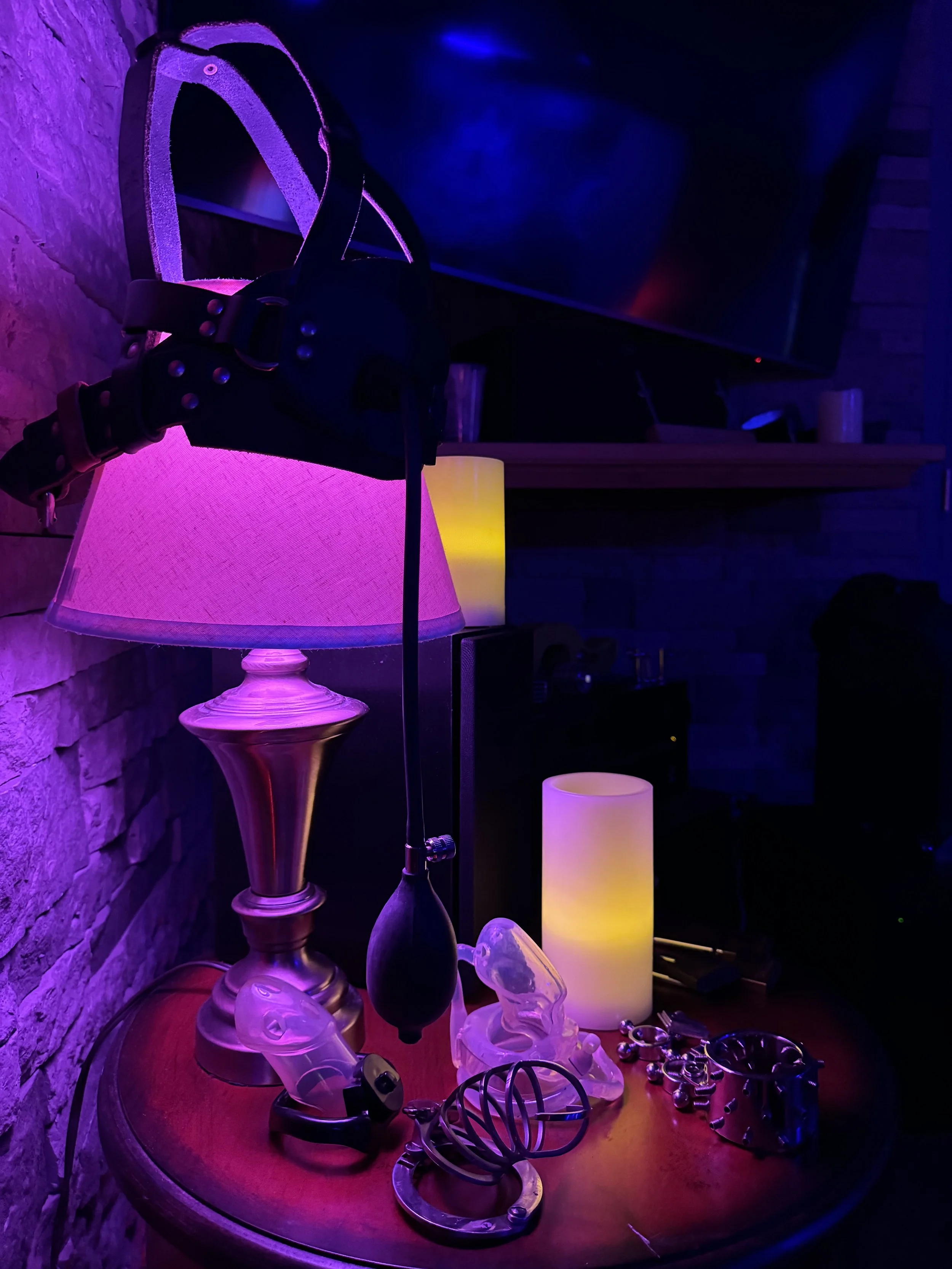 A wooden table with a lava lamp, decorative glass objects, jewelry, and a bracelet, illuminated by purple and yellow lighting in a dim room.