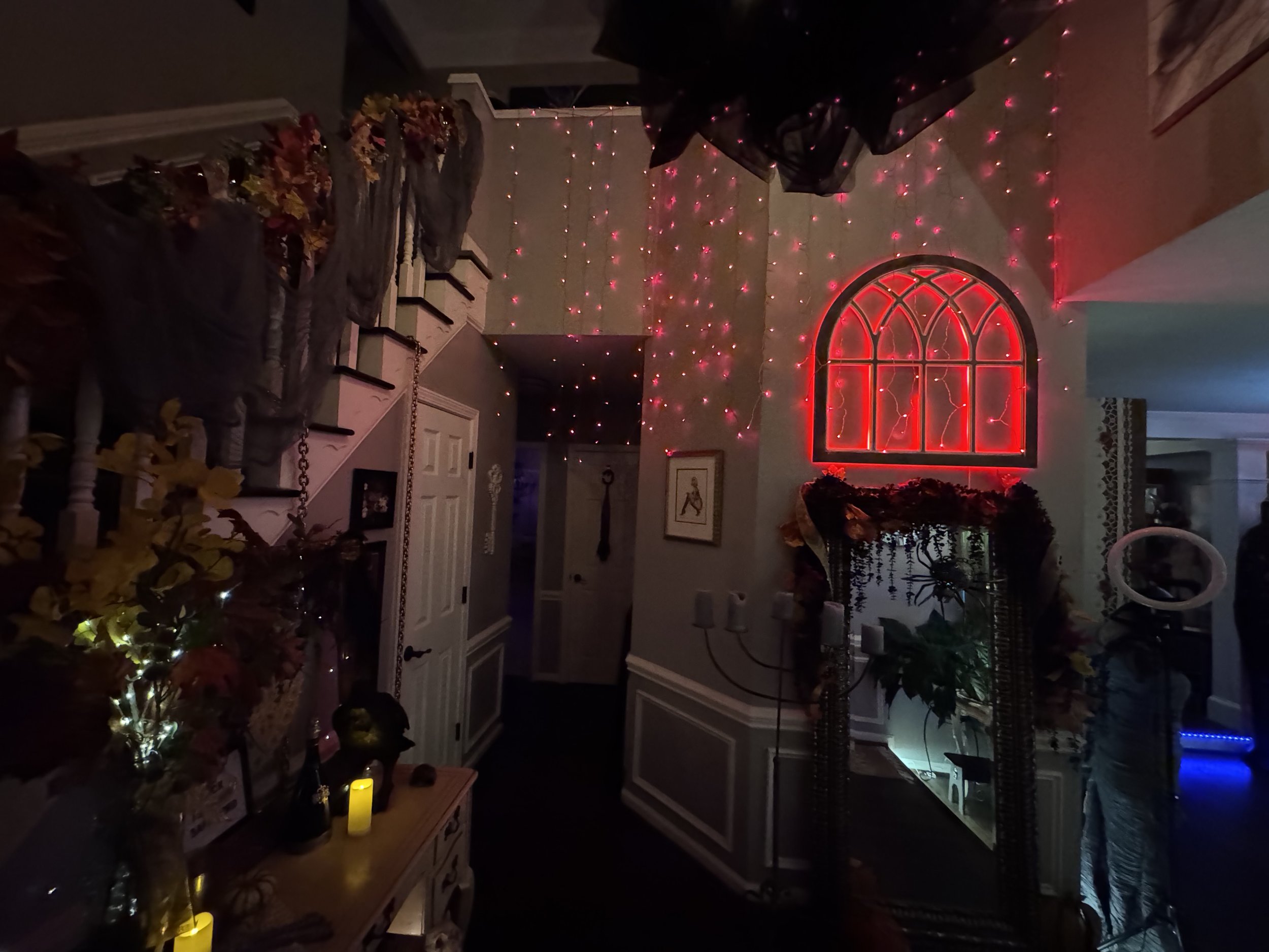 Decorated interior with red neon window lights, pink string lights, floral arrangements, candles, and picture frames in a dimly lit room.