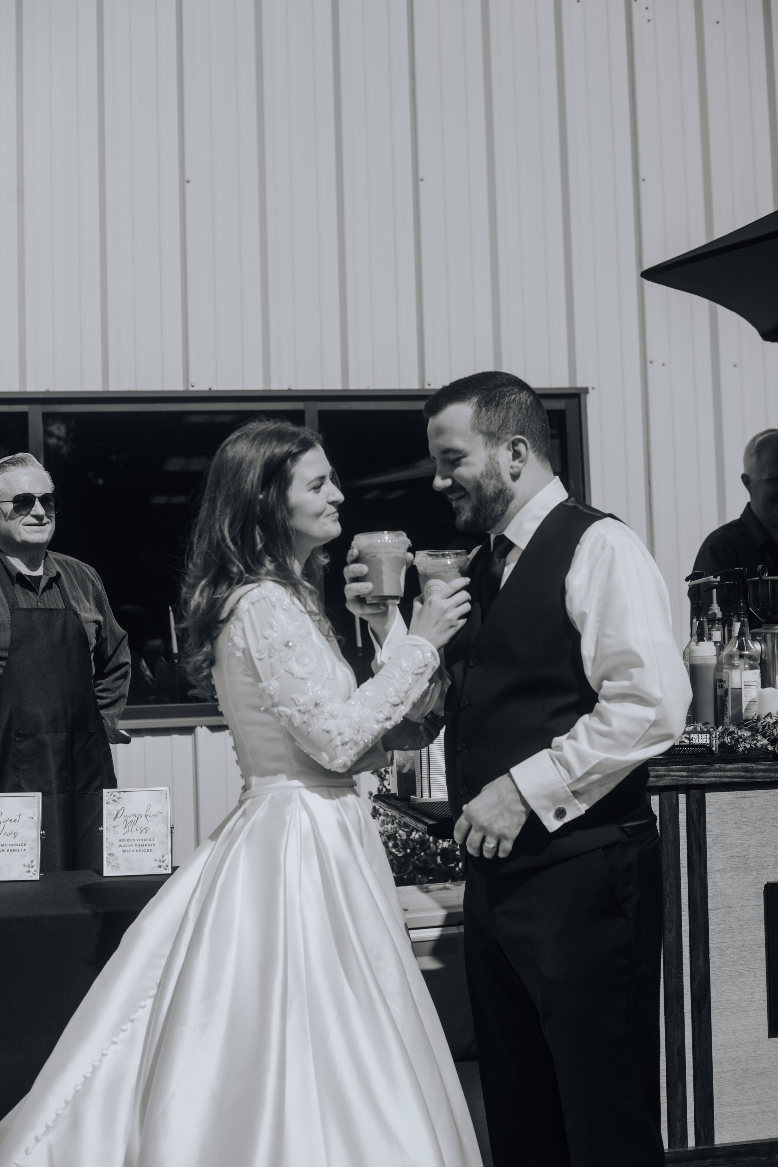 A black-and-white photo of a bride and groom smiling and holding drinks at their wedding reception.