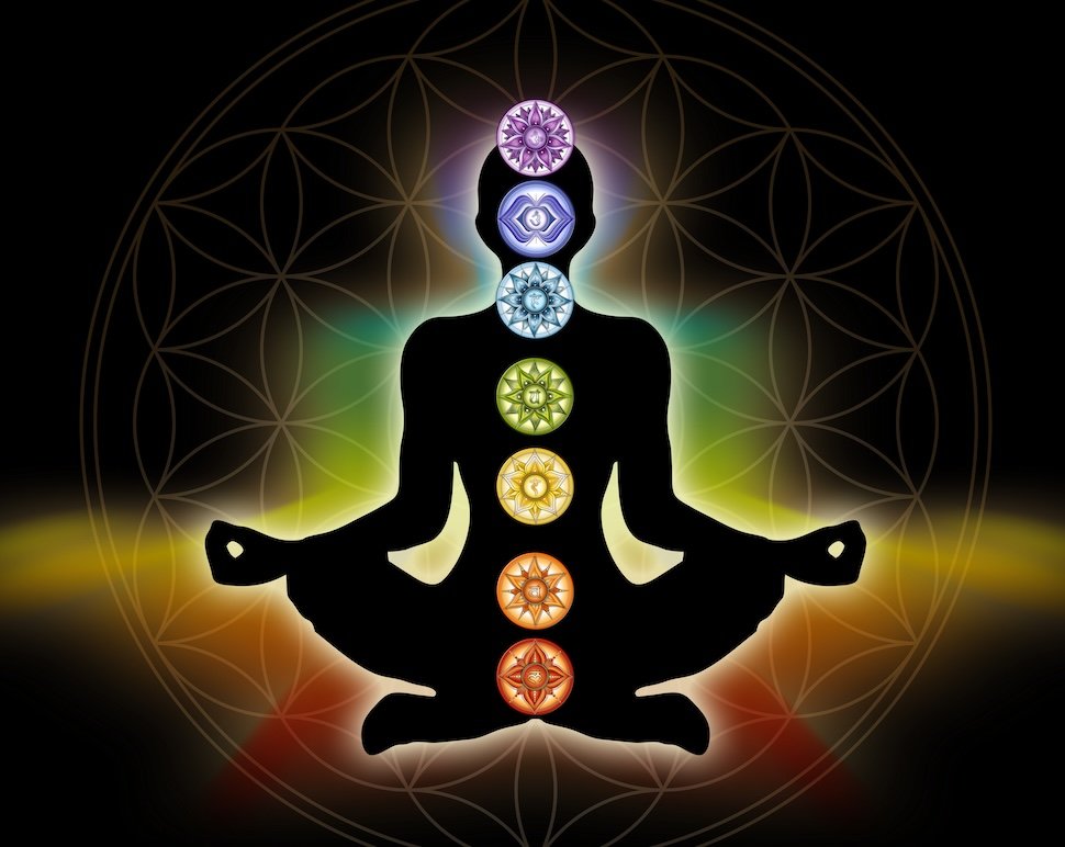 Silhouette of a person sitting in a lotus position with seven colorful chakras aligned vertically along their body, against a dark background with a geometric circle pattern.