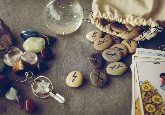A collection of runes, tarot cards, a glass orb, and various crystals on a surface used for divination.