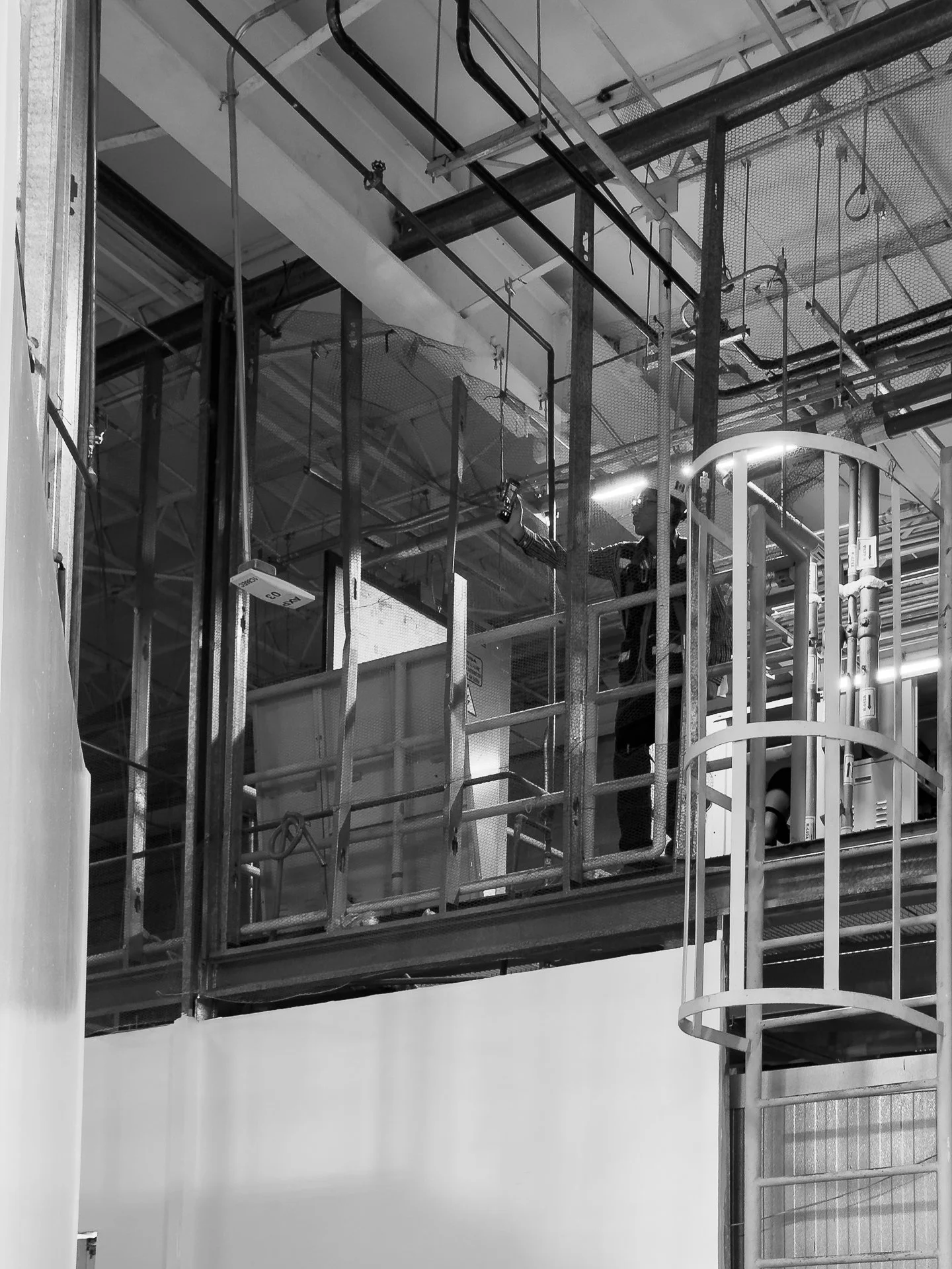 Una persona limpiando una estructura de metal en un área industrial, usando protección ocular y de seguridad.