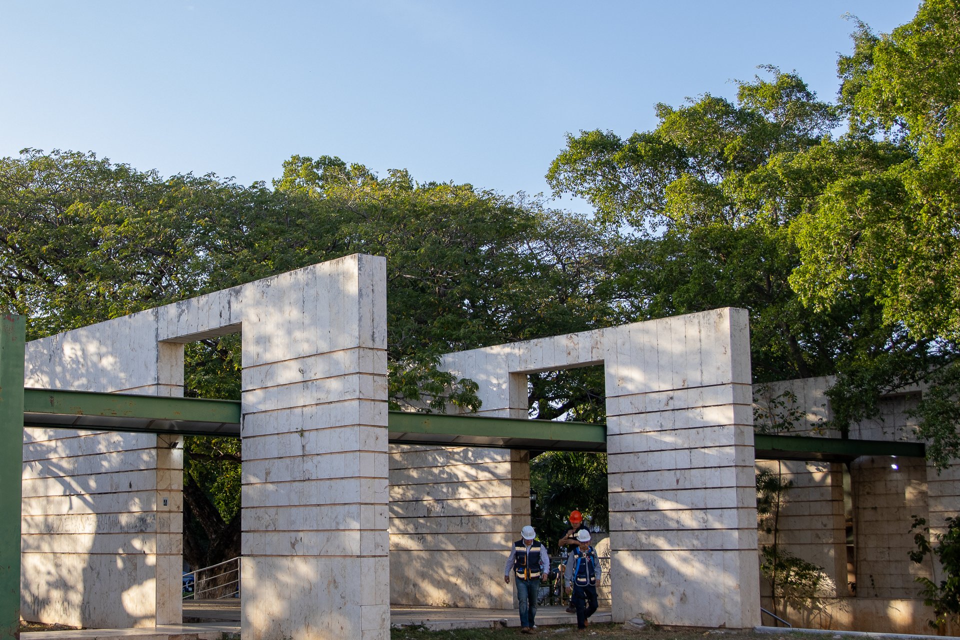 Personas con cascos en una construcción en marcha, rodeadas de árboles y estructuras de piedra blanca.