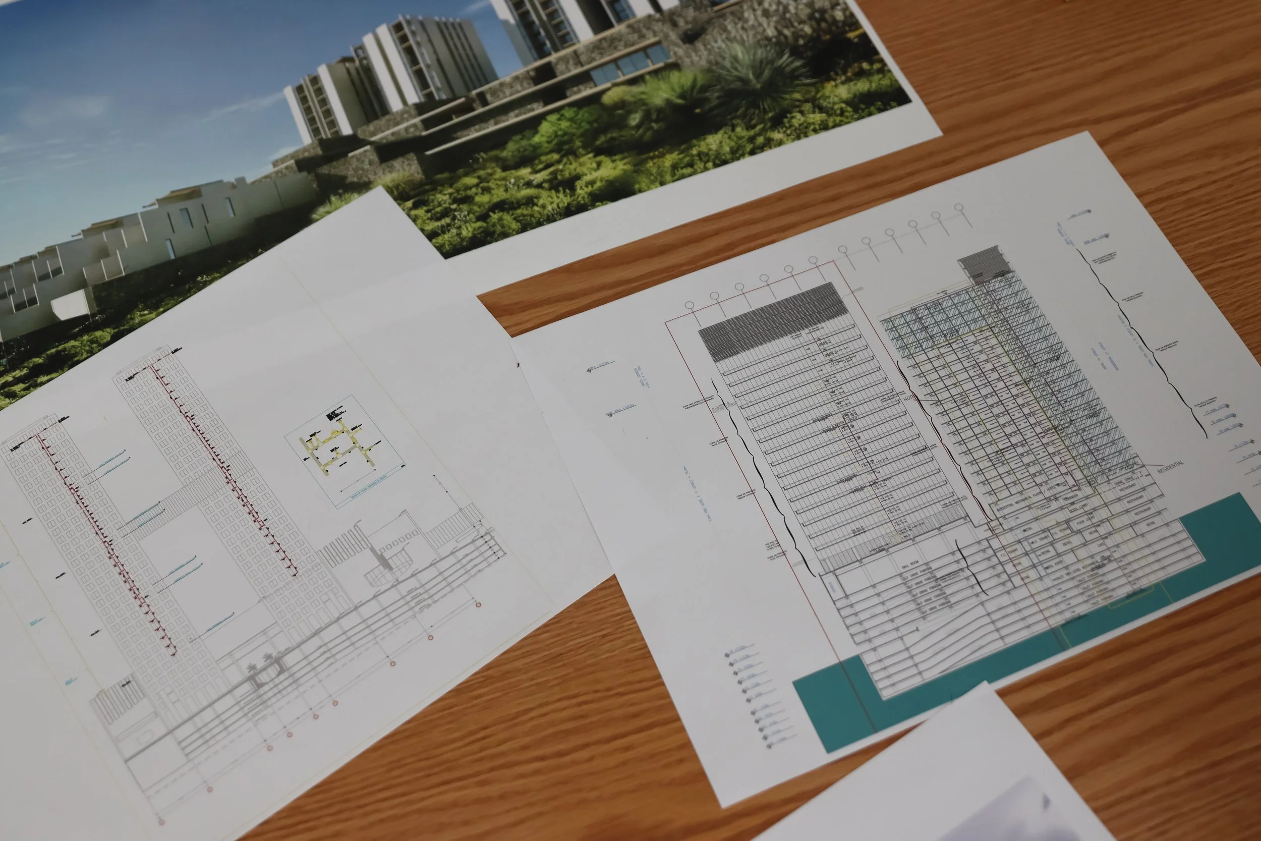 Planos arquitectónicos y una imagen de un edificio moderno con jardines en la azotea sobre una mesa de madera.