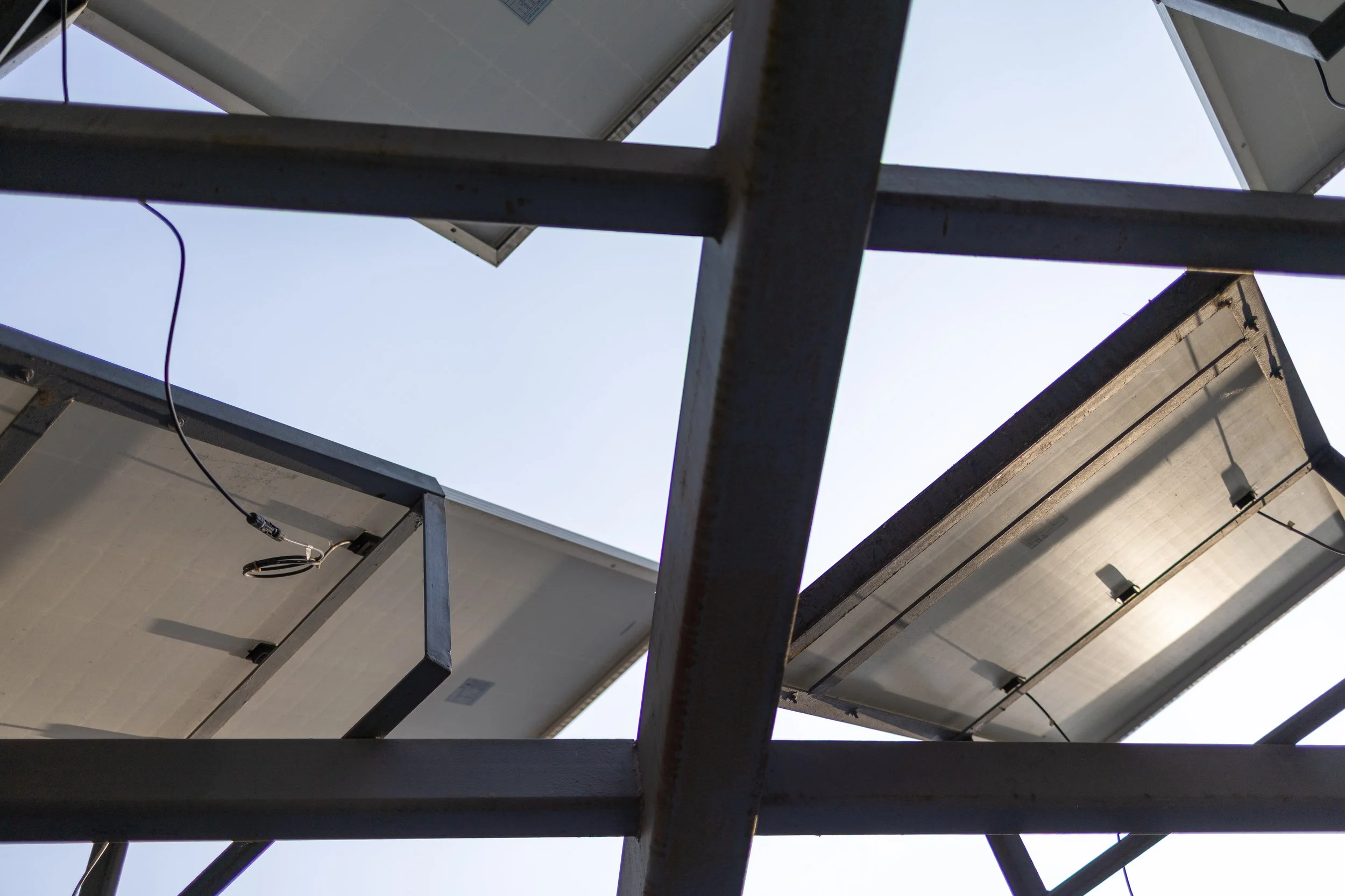 Paneles solares instalados en una estructura metálica vista desde abajo, con cielo despejado en el fondo.