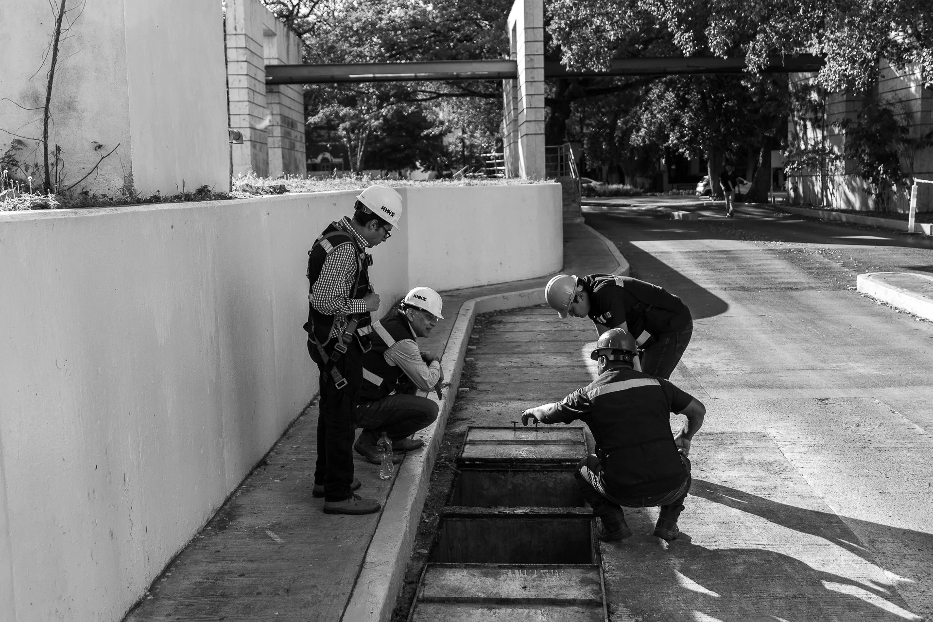 Cinco trabajadores con cascos revisando una abertura en la acera en una calle de ciudad.