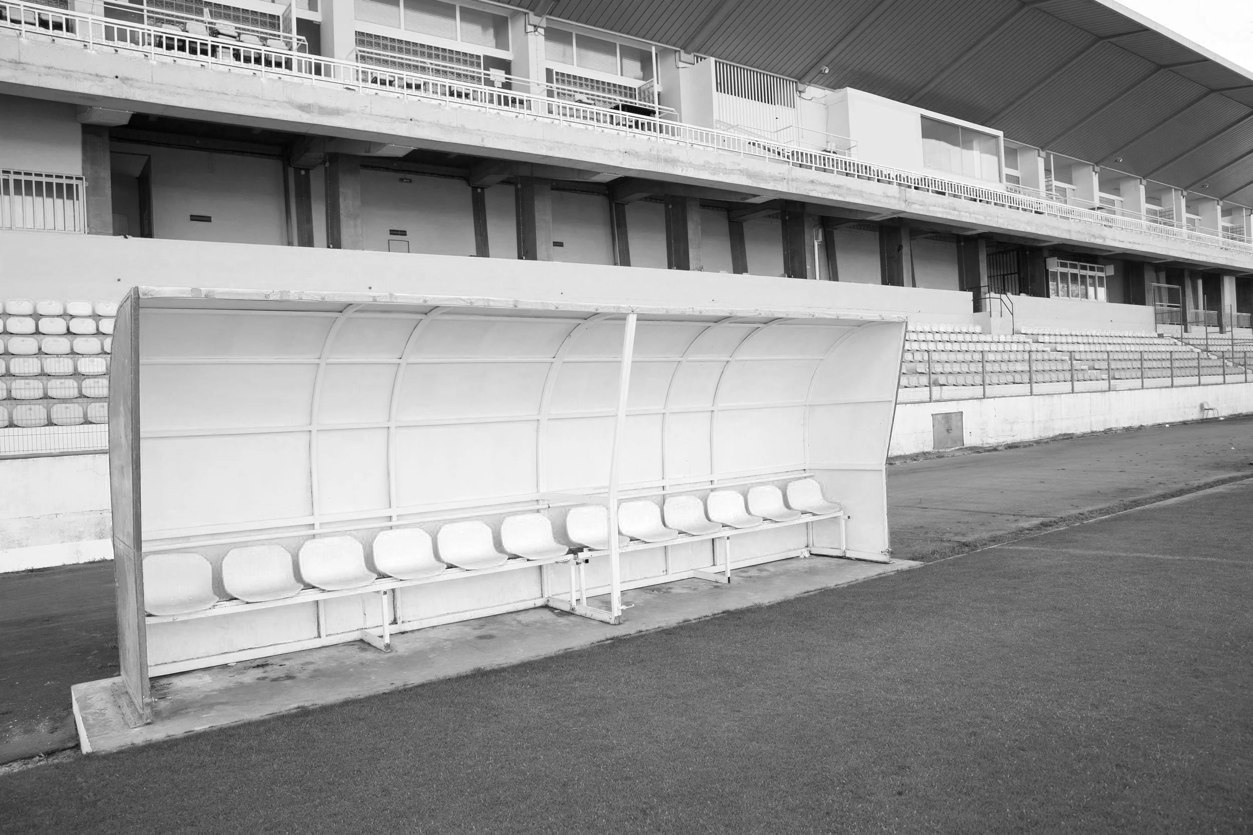 Imagen en blanco y negro de una banca de suplentes en un campo de fútbol.