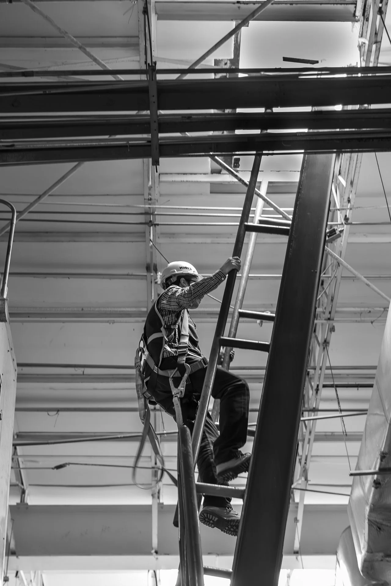 Persona trabajando en construcción en una estructura de andamios, usando casco y arnés de seguridad.