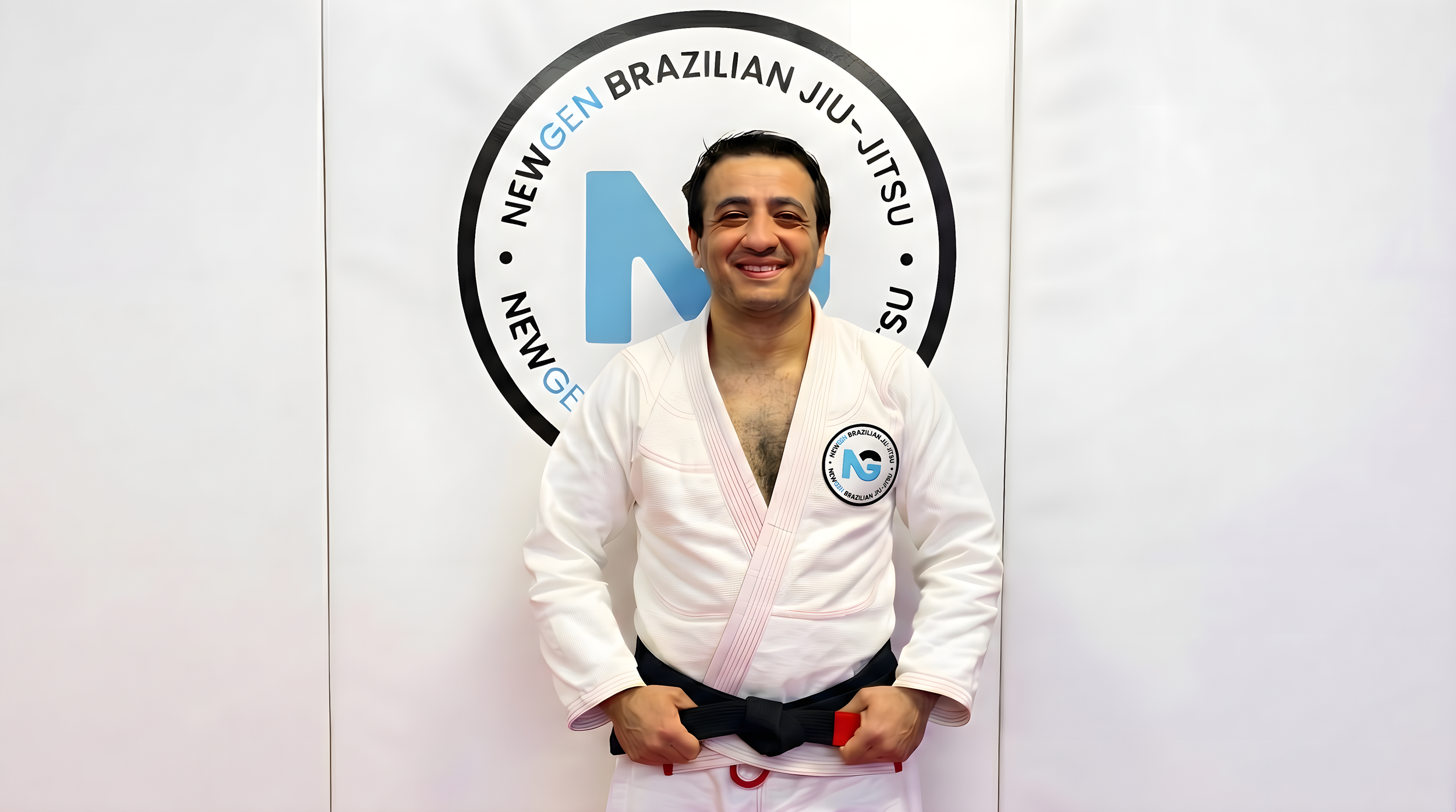Man smiling in Brazilian Jiu-Jitsu uniform standing in front of a logo for Newgen Brazilian Jiu-Jitsu.
