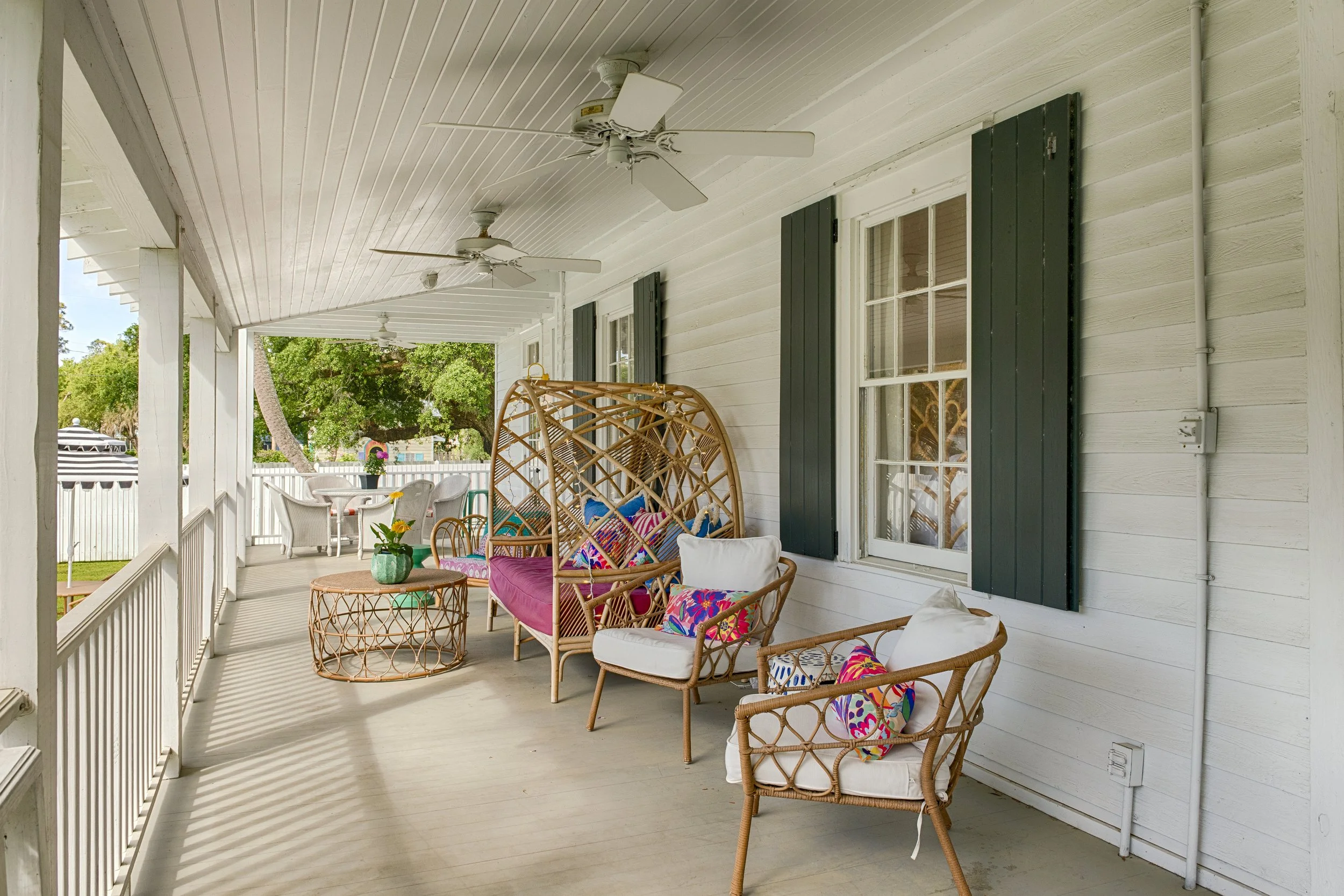 One of four inviting porches at Bliss Cottage on Tybee Island, featuring cozy seating, vibrant colors, and a view of lush greenery.