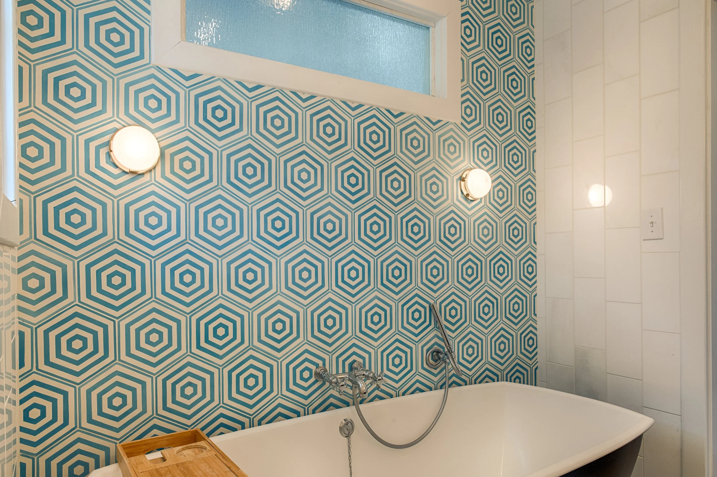 Soaking tub in the primary suite of Bliss Cottage on Tybee Island, featuring bright natural light, white tile surround, and serene coastal decor.