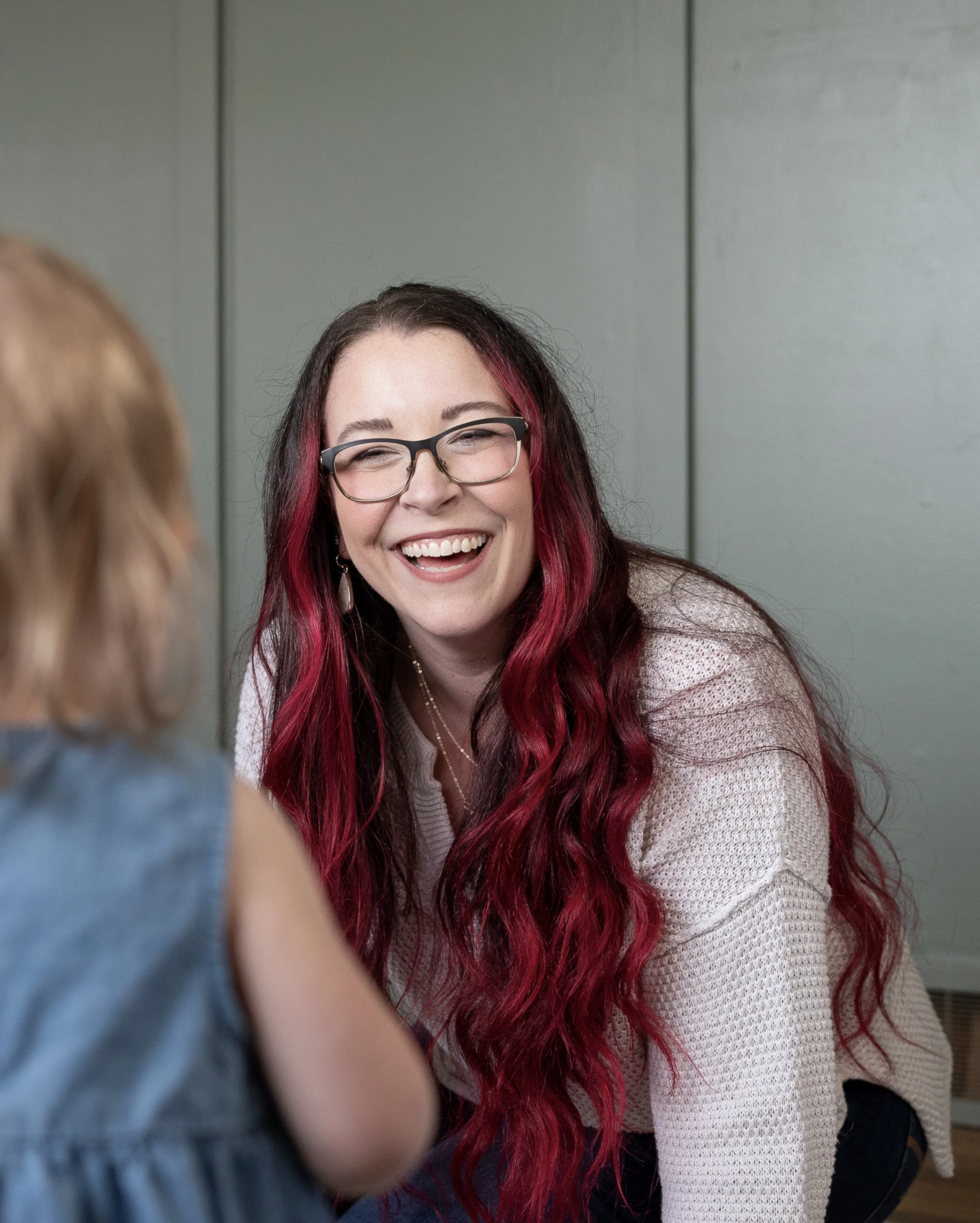 Mom laughing as her daughter walks toward her playing with music toys—faith-based motherhood and music at home