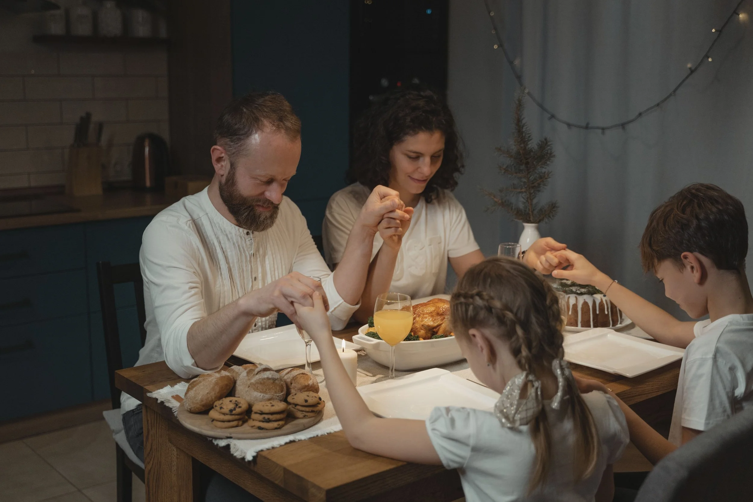 Family holding hands and praying together around the dinner table before sharing a meal.