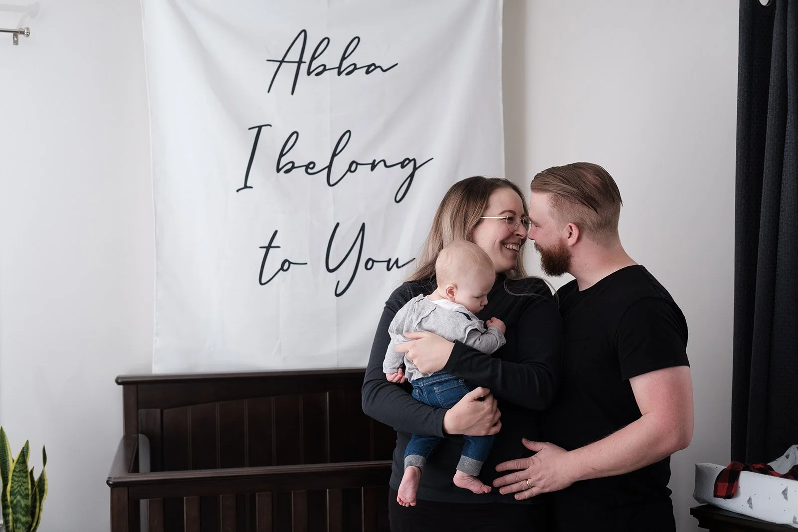 Parents holding their baby son in his bedroom with a banner reading ‘Abba I belong to you’