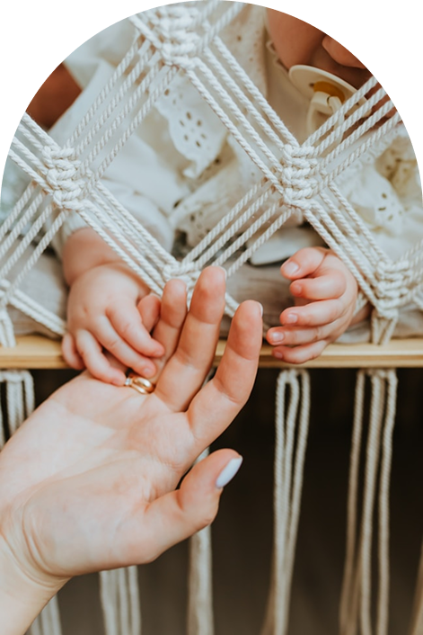 Mom holding baby’s hand through a woven crib as baby uses a pacifier—peaceful bedtime routine for a faith-filled home