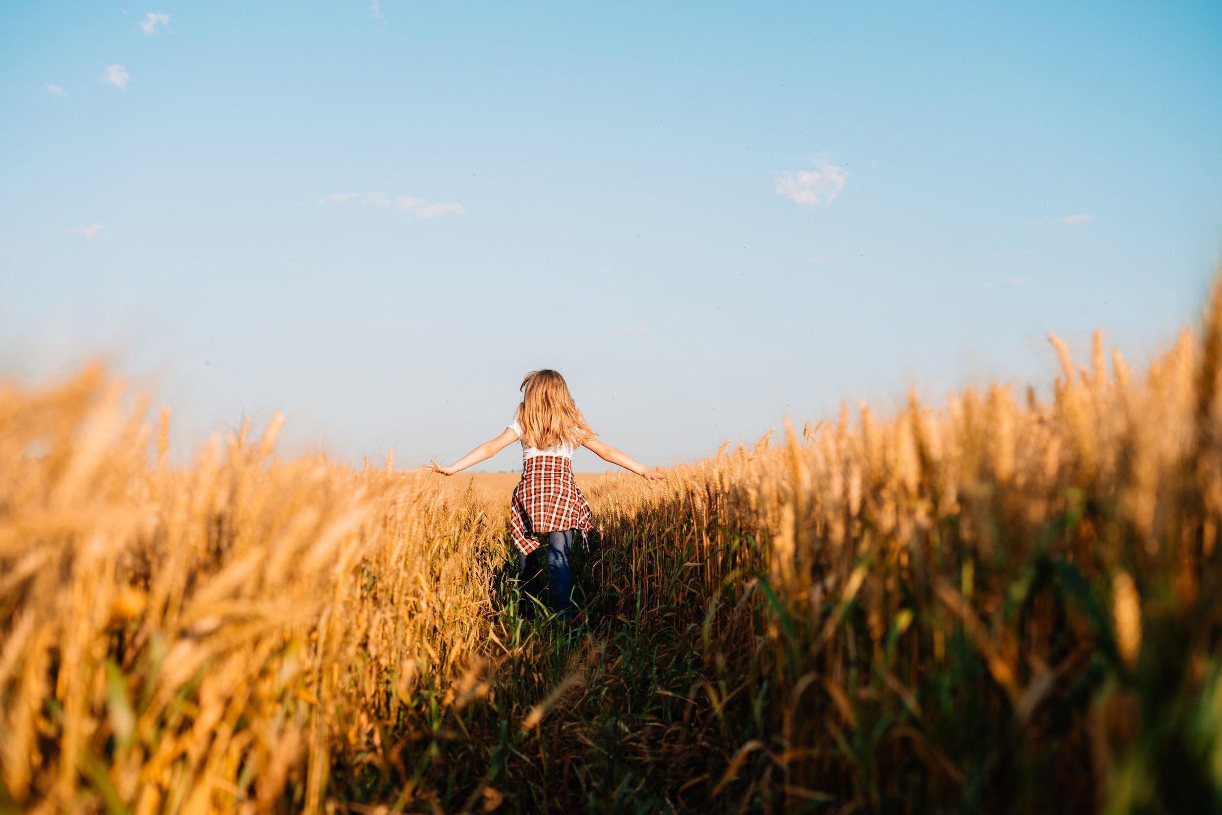 Woman running through a cornfield with her arms outstretched, enjoying a peaceful moment outdoors.