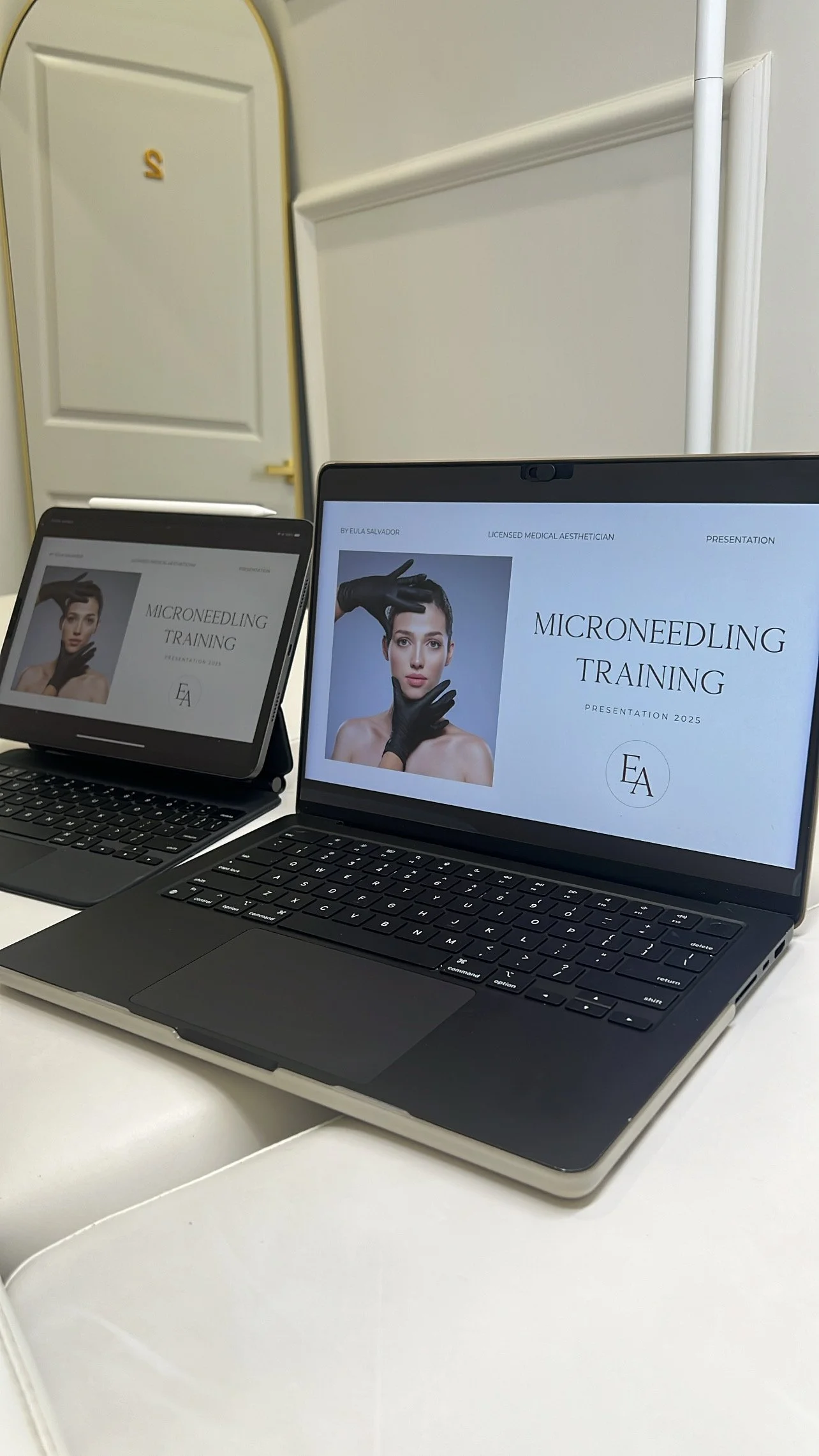 Two laptops on a white table displaying slides for a microneedling training presentation, with a door in the background.