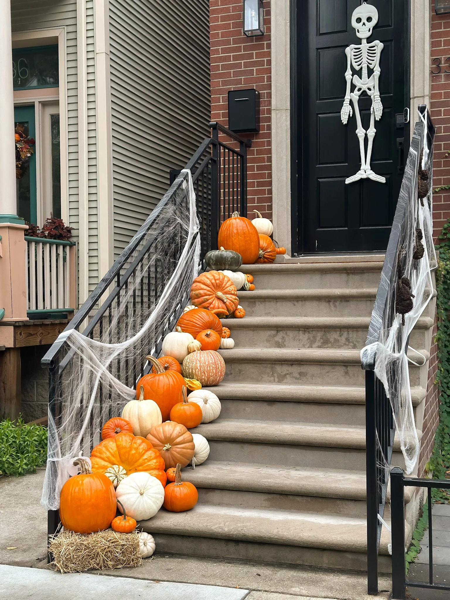 Decorative pumpkins and gourds arranged along the front steps of a house with a wreath on the door, autumn plants, and potted plants on the landing.