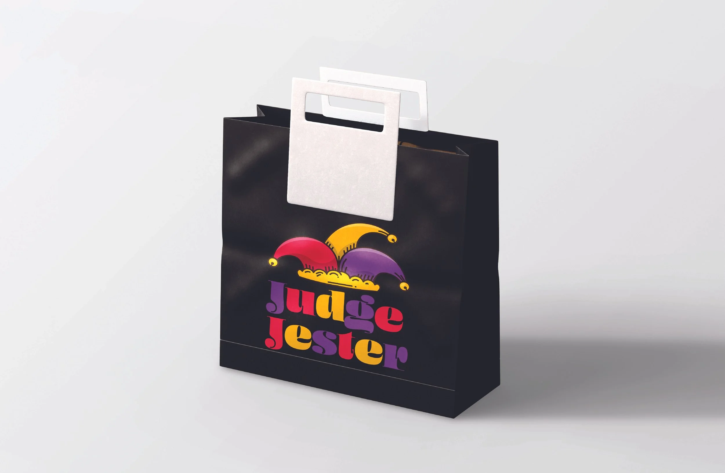 A black shopping bag with colorful text that reads 'Judge Jester' and jester hat graphics, with white and transparent handle attachments, is placed against a plain white background.