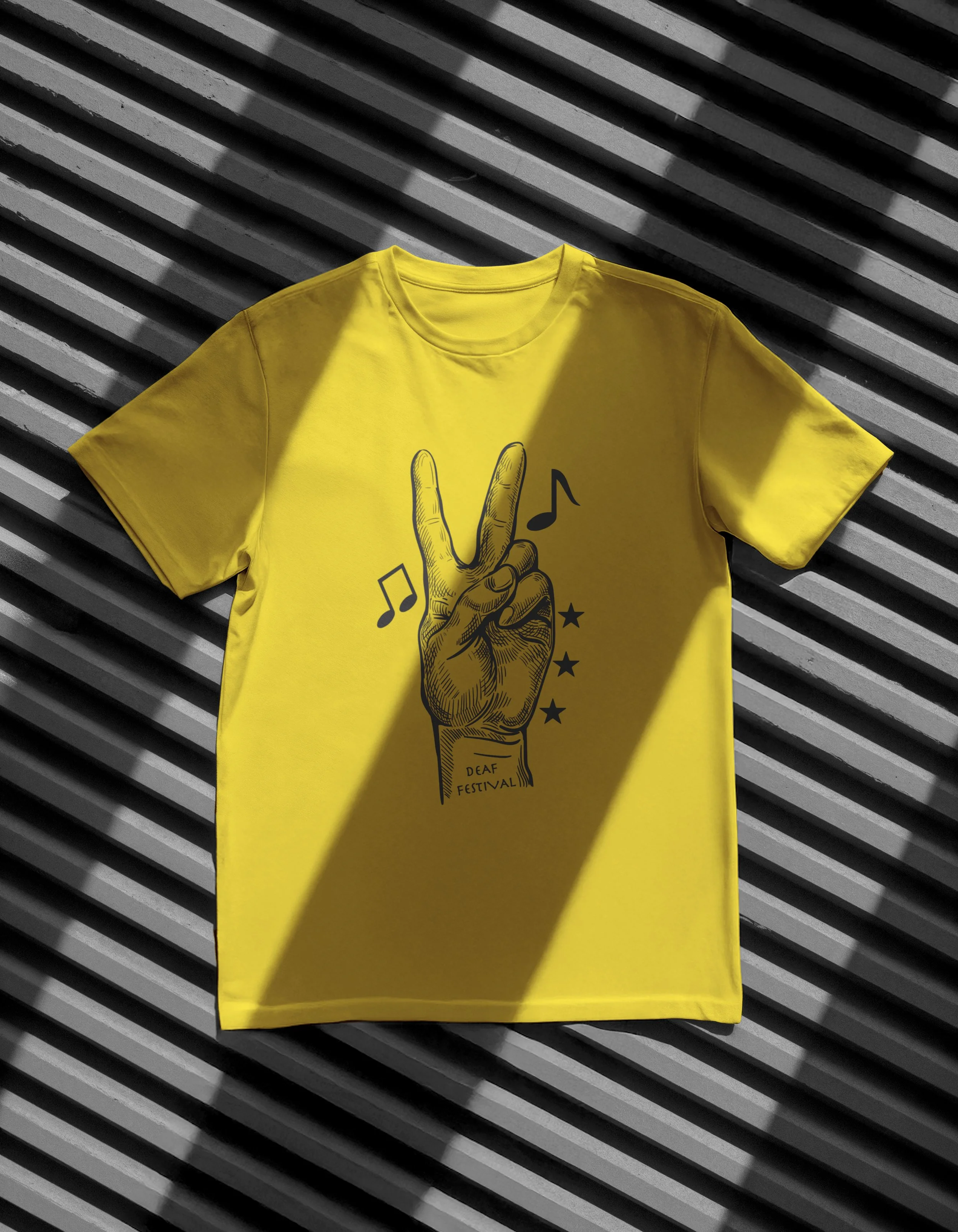 Yellow T-shirt with a black printed graphic of a hand making a peace sign and musical notes, placed on a diagonally striped surface.