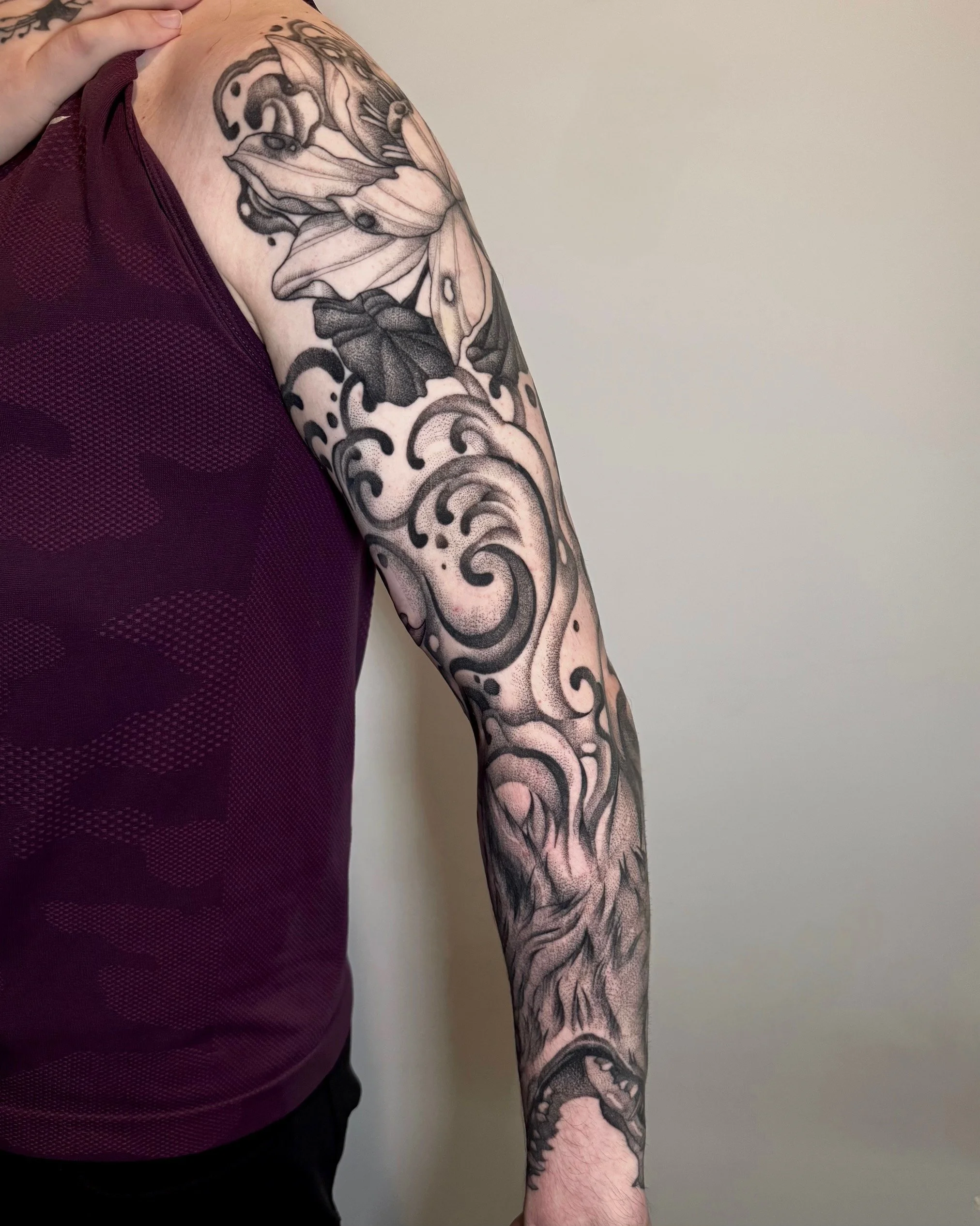 Black tattoo sleeve featuring a butterfly, waves, a wolf, and a snake on a person's arm.