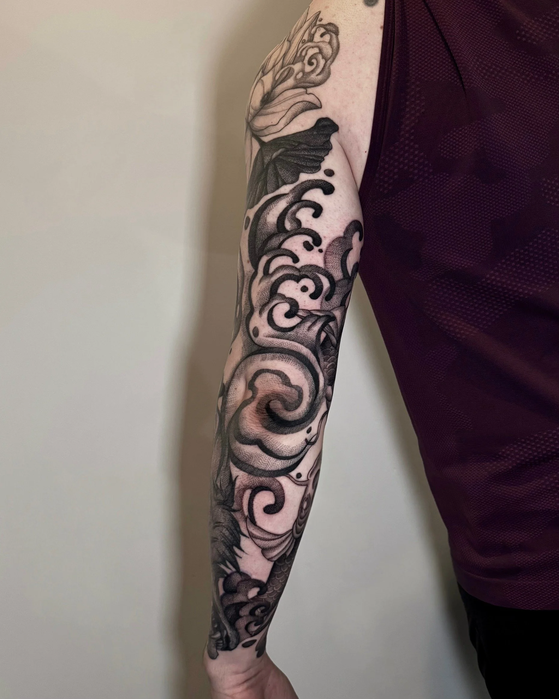 Black and gray tattoo sleeve featuring waves and clouds on a person's arm.