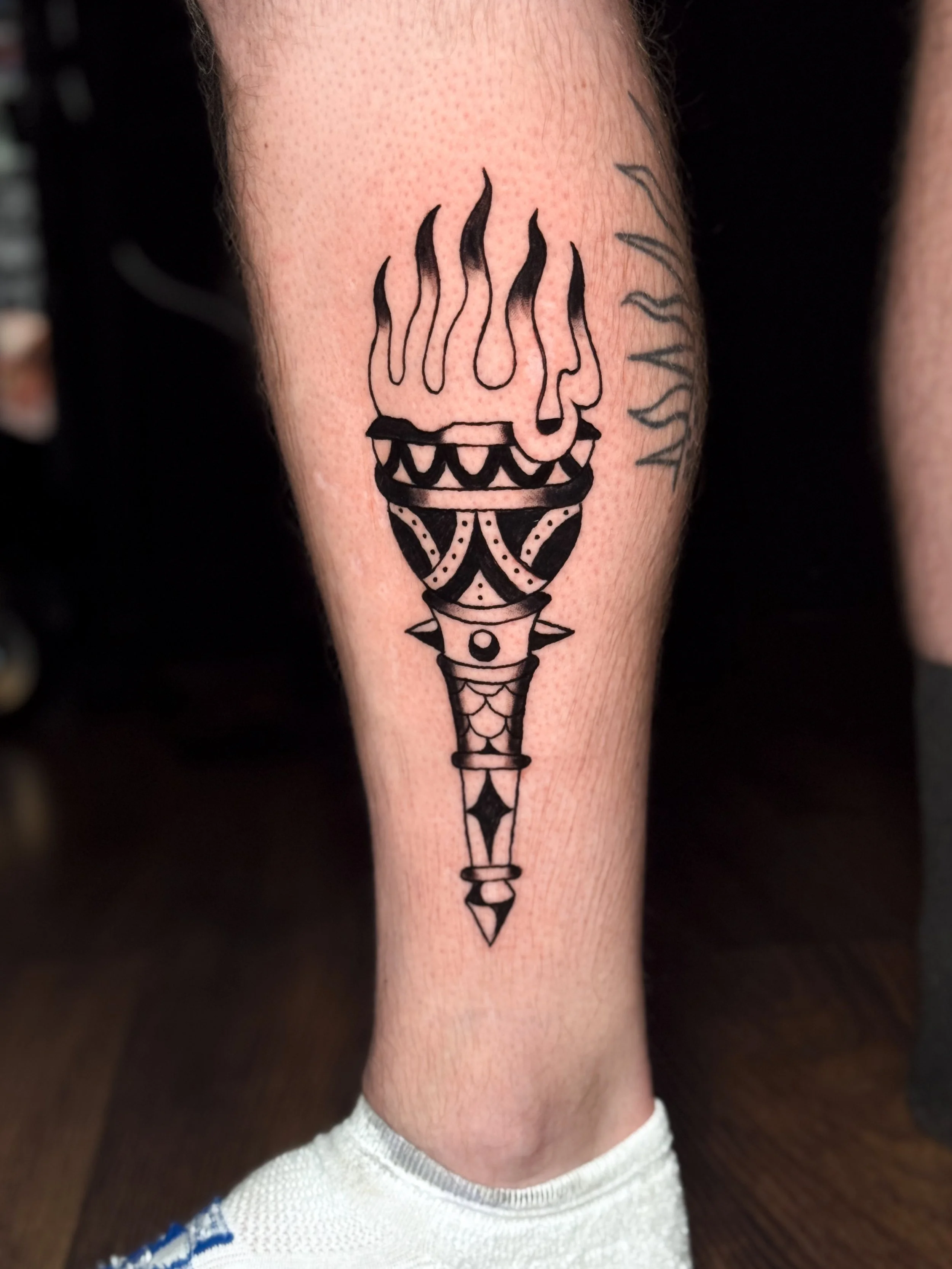 Black line tattoo of a torch with flames on the forearm of a person.