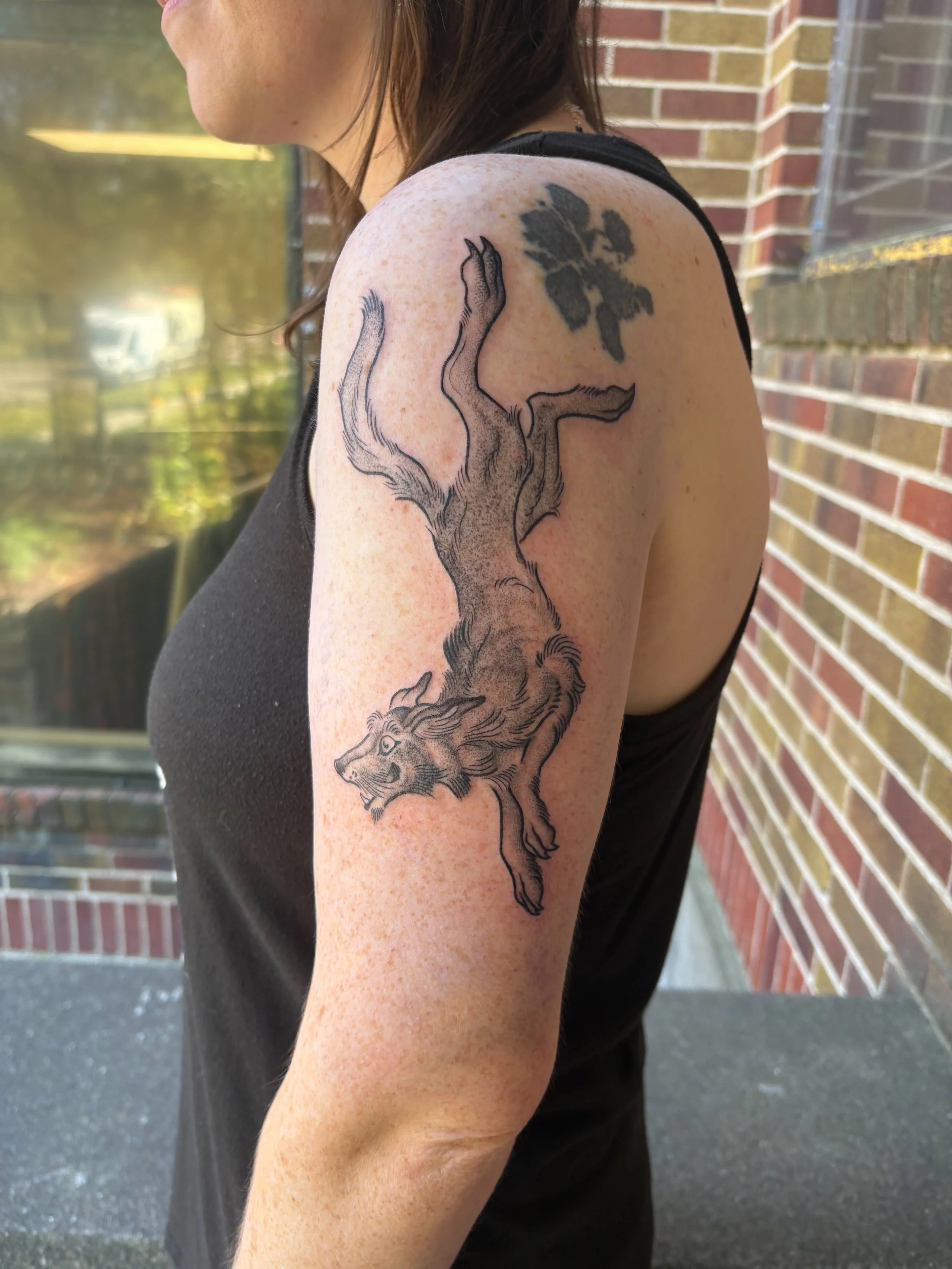 Tattoo of a leaping lion on a woman's upper arm with a leaf design near the shoulder.