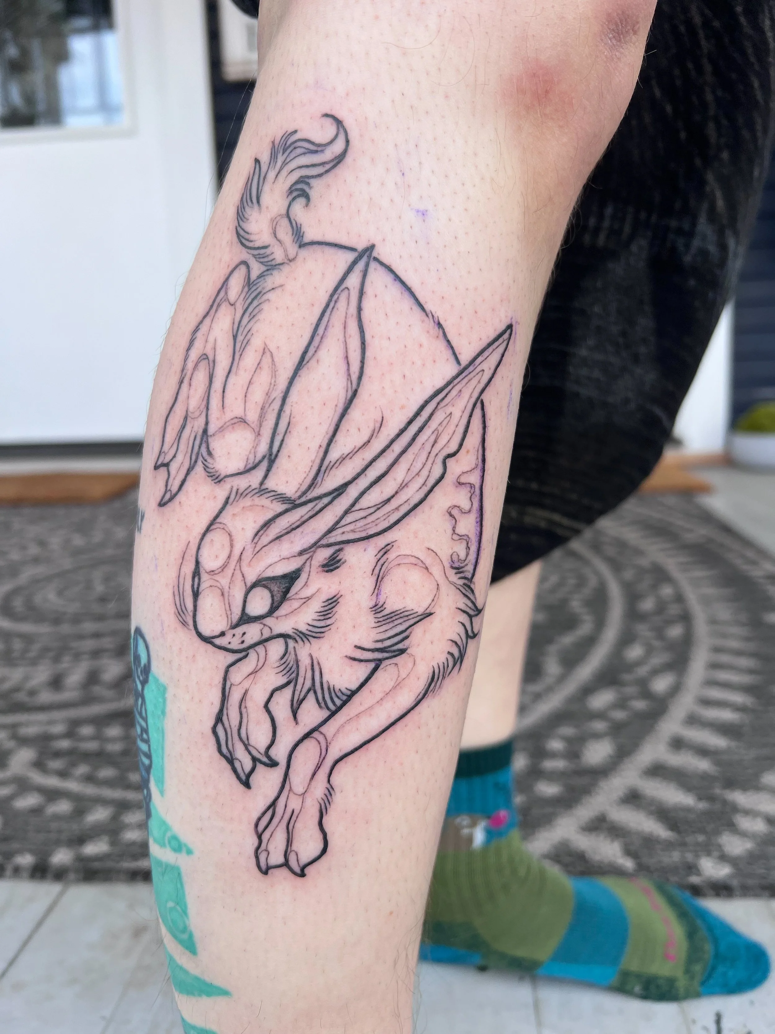 Line art tattoo of a rabbit with wings on a person's calf.