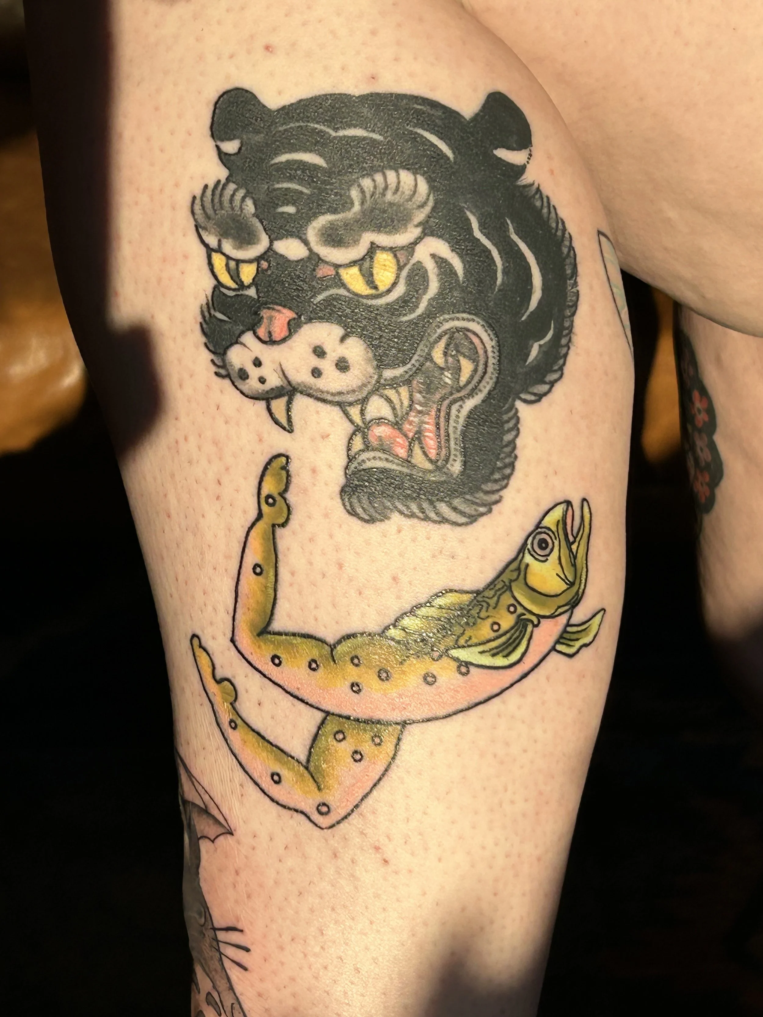Tattoo of a panther head above a fish on a person's arm.