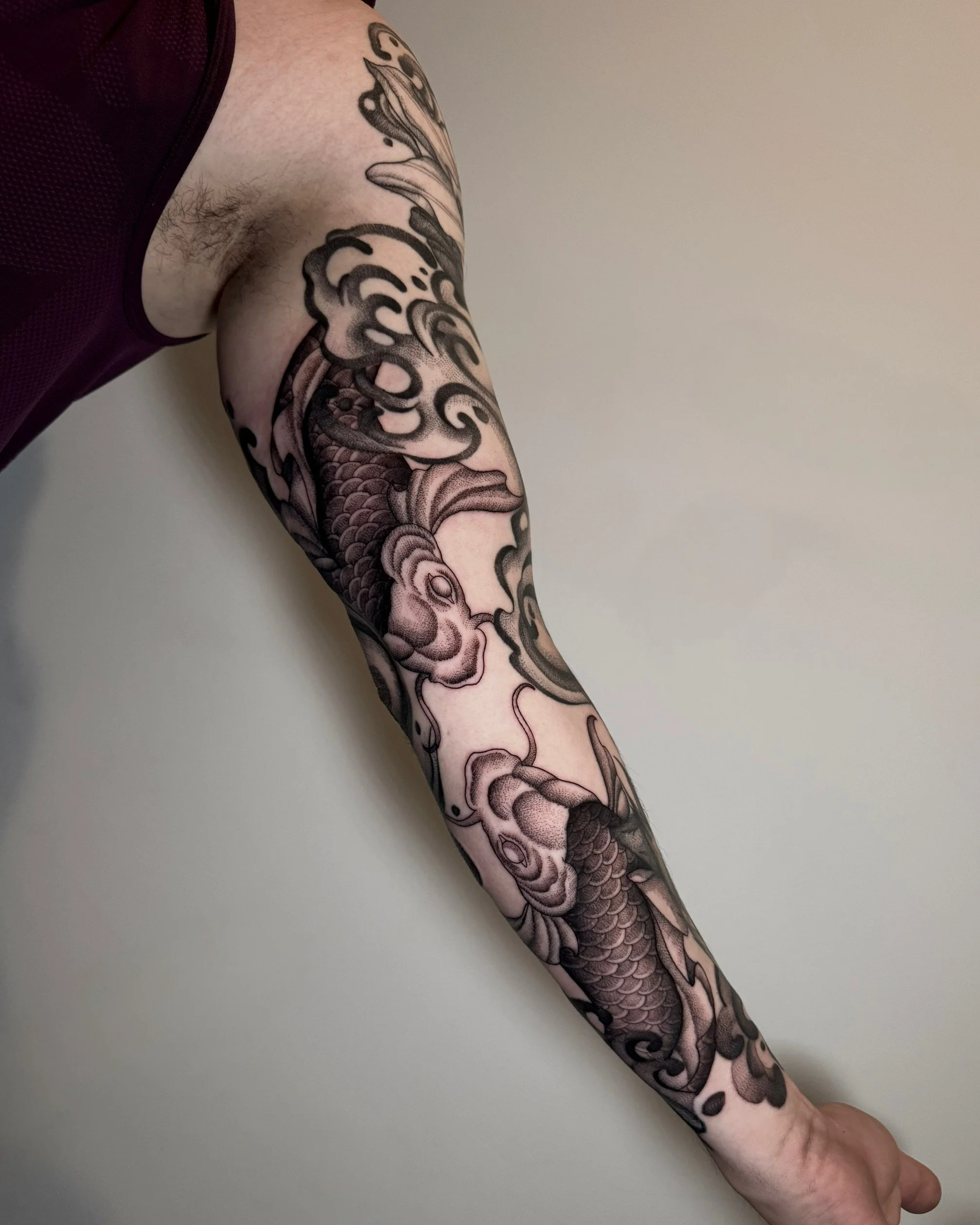 Black and gray tattoo of a koi fish surrounded by clouds on a person's arm.