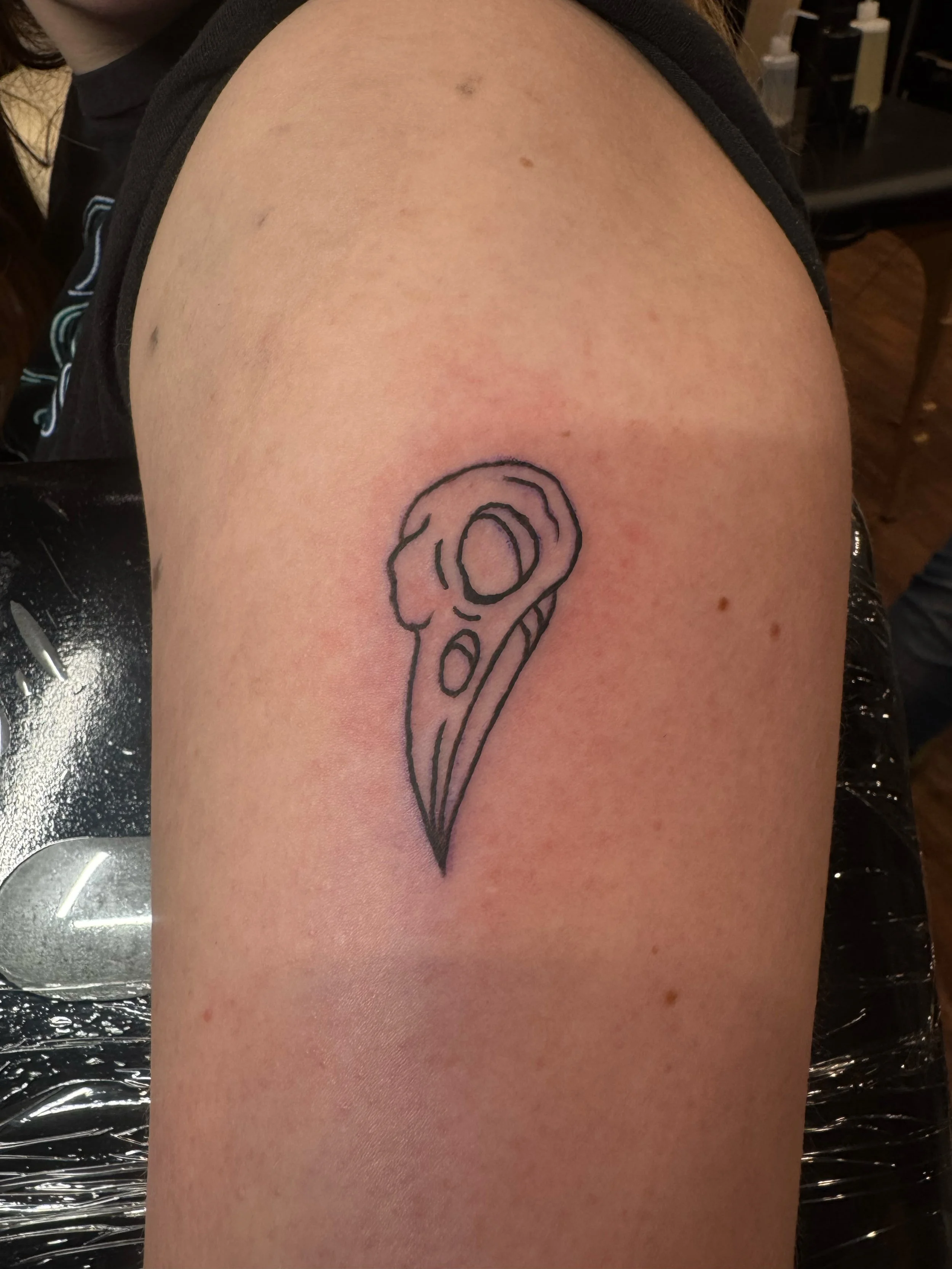 Tattoo of a stylized pizza slice on person's upper arm.