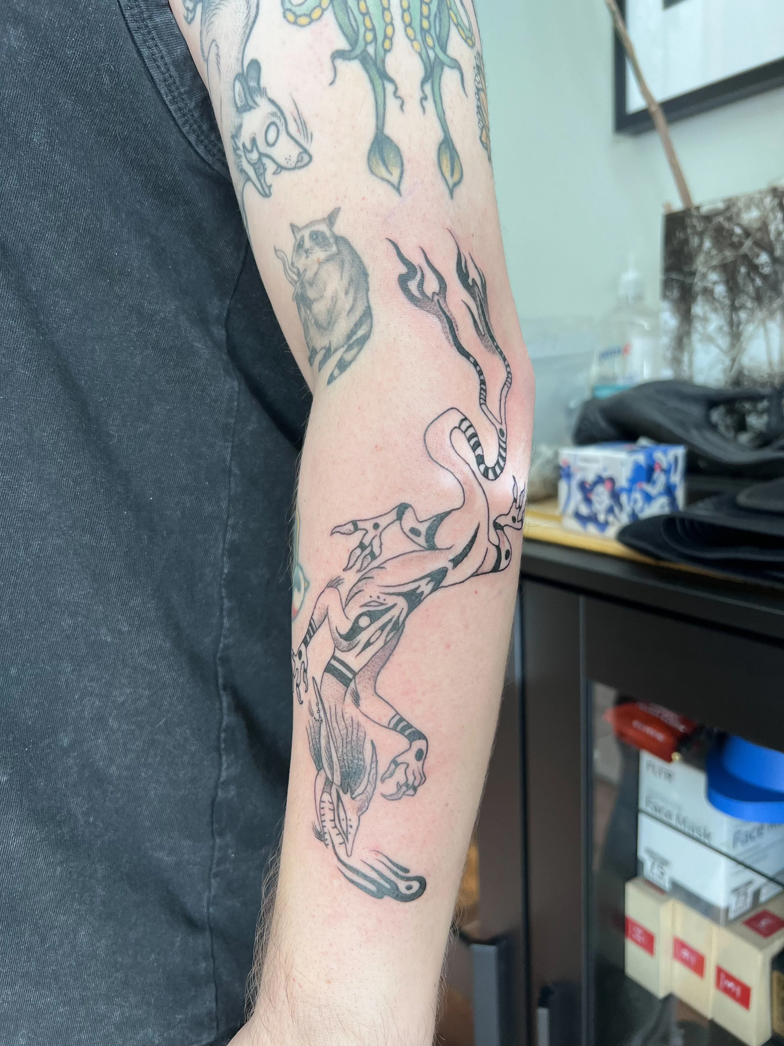 Tattoo of a stylized, black and gray unicorn on a person's arm, with flames coming from its mouth, on a person's forearm.