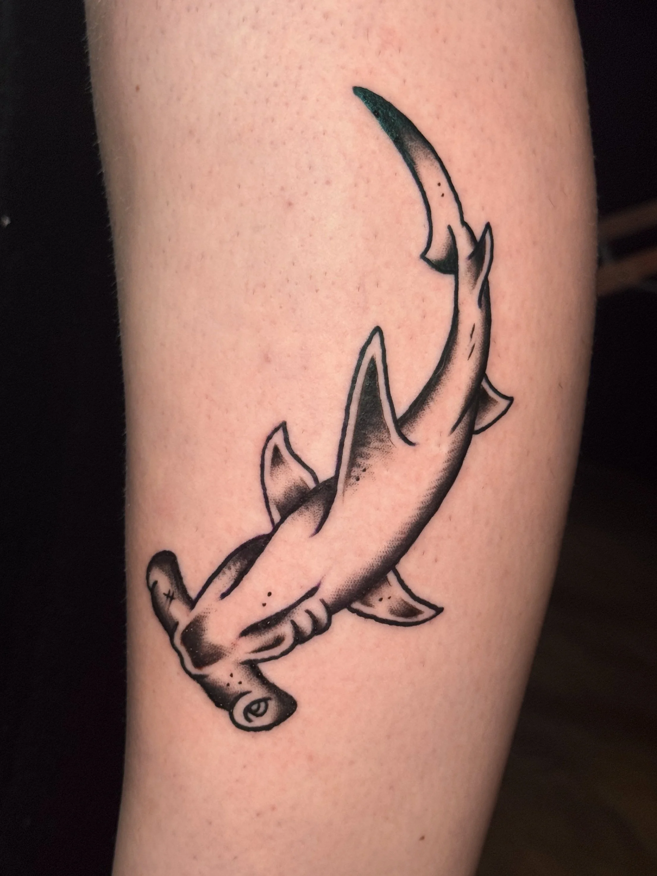 Tattoo of a shark's fin and tail on a person's arm.