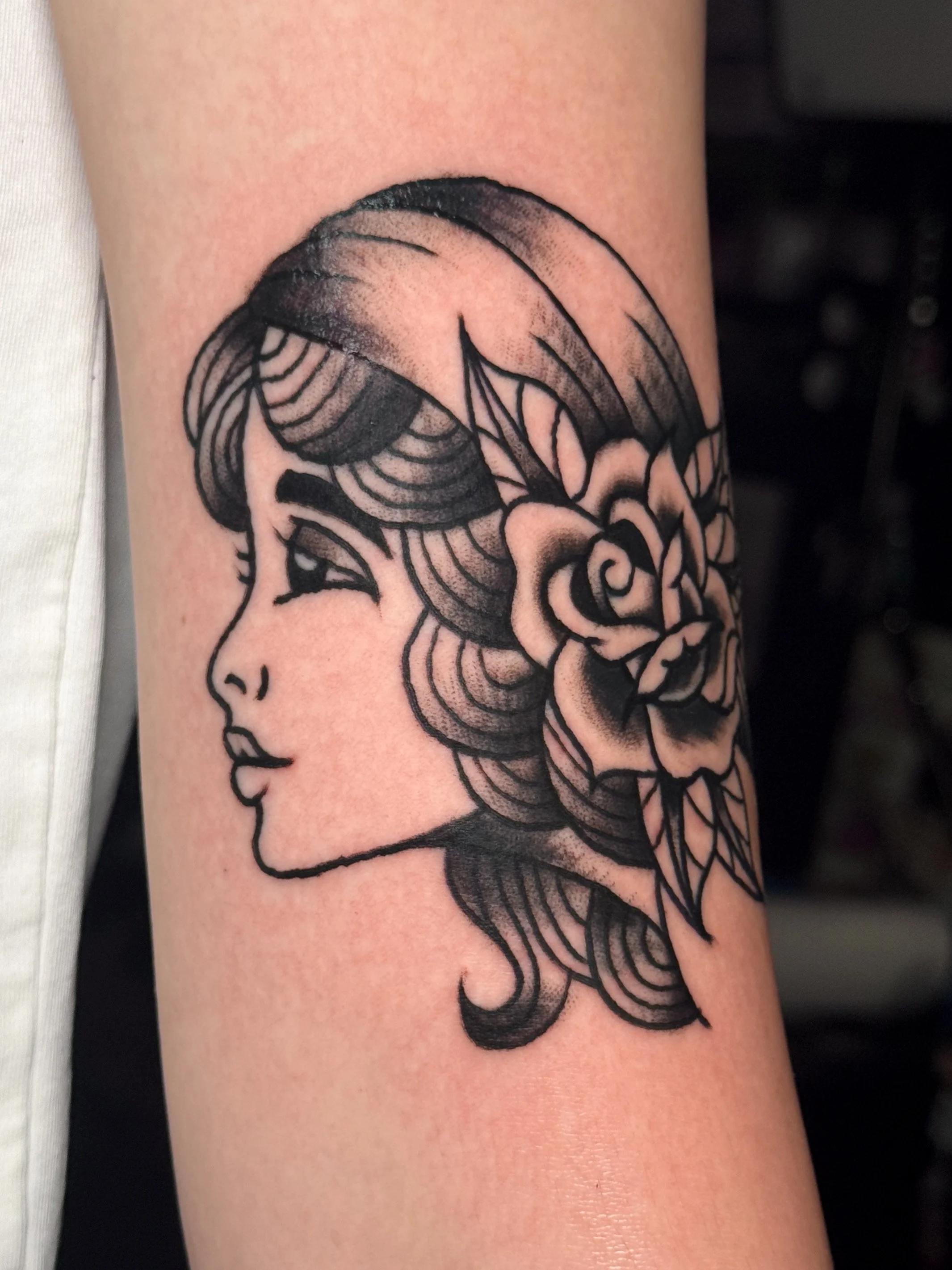 Black tattoo of a woman's face in profile with flowing hair on person's arm.